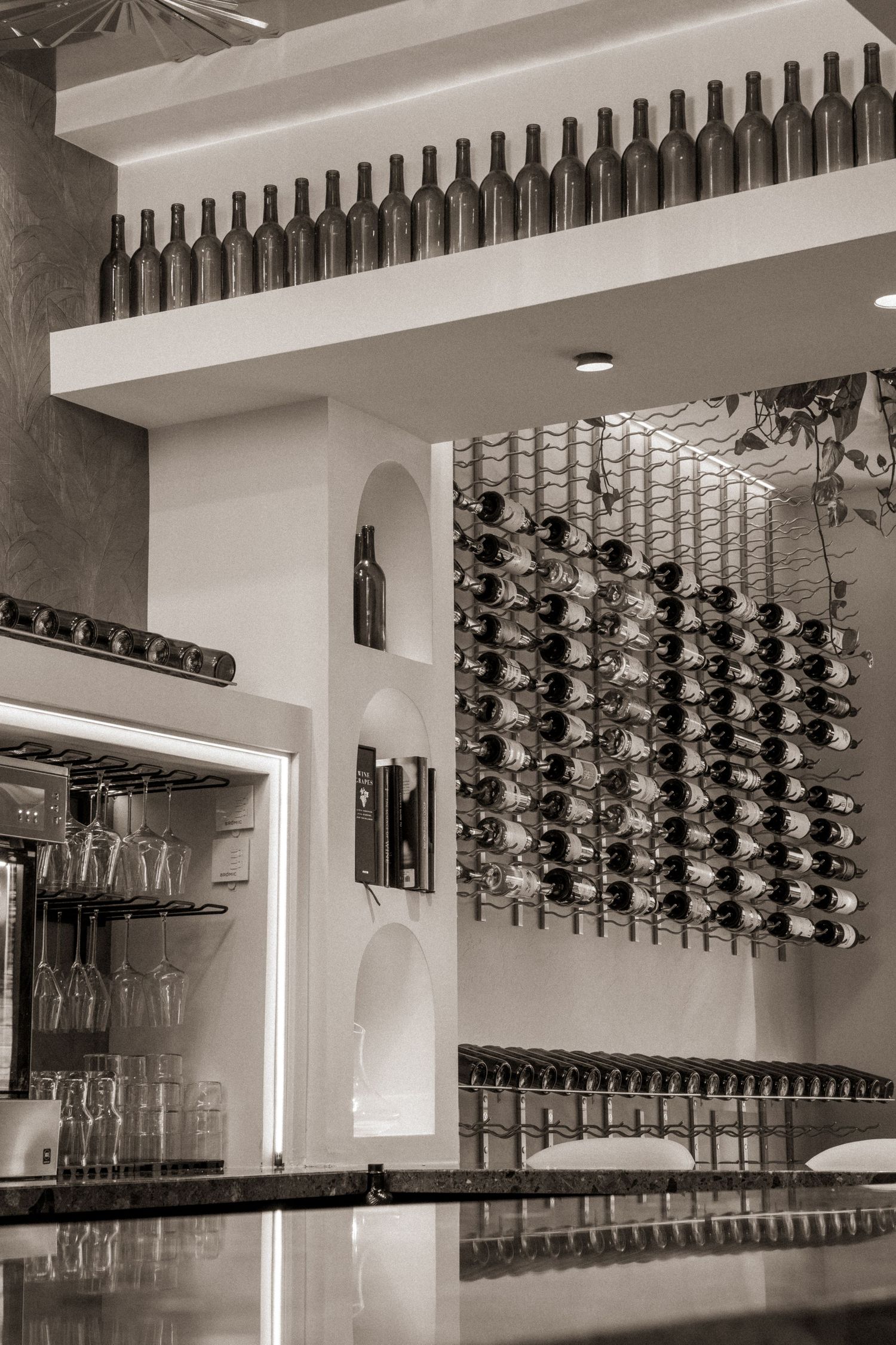 Black and white photo of wine bar interior with bottle display wall, wine racks, and stemware storage.