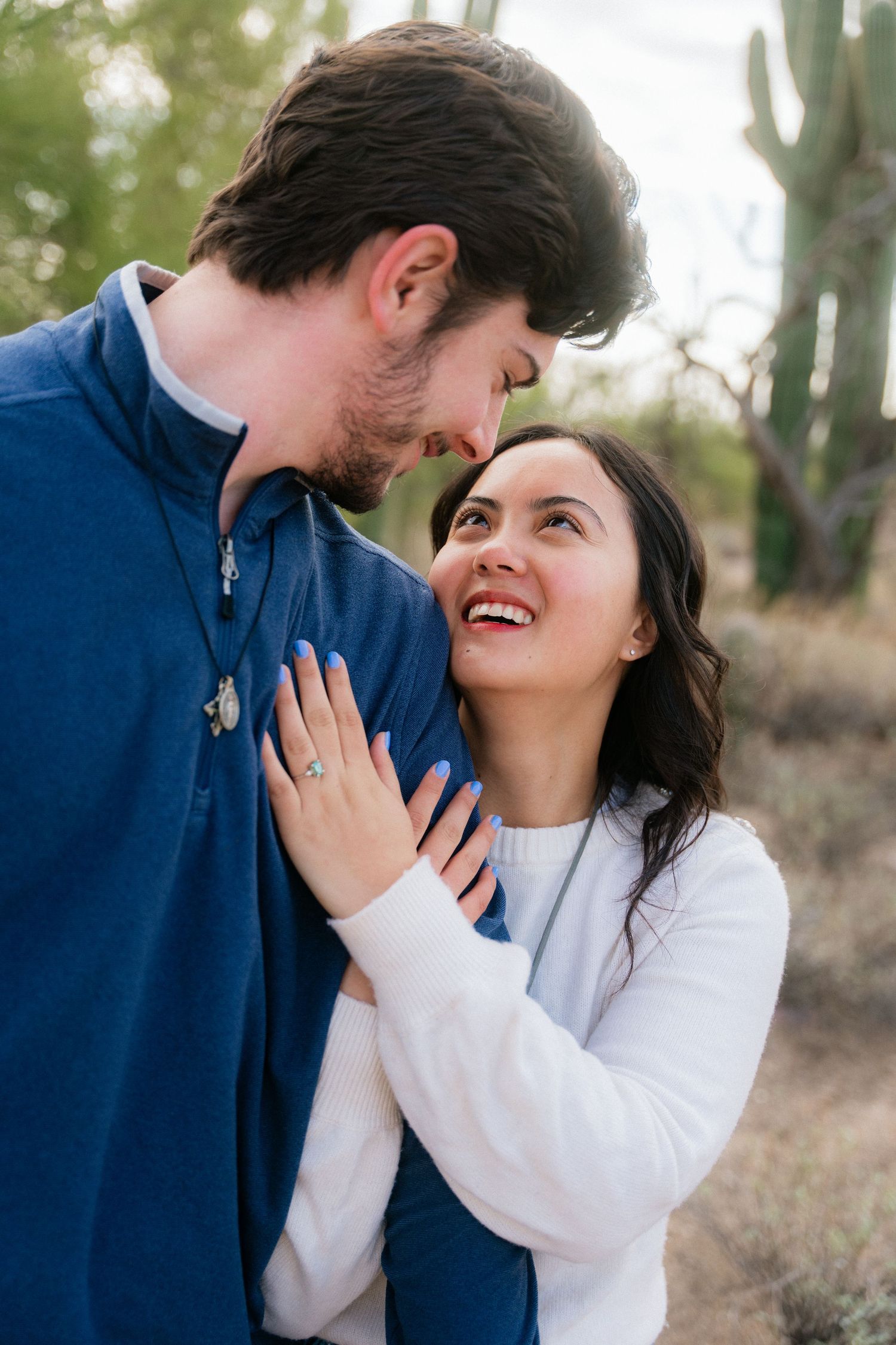 A woman laughs joyfully while embracing a man outdoors in a desert landscape.