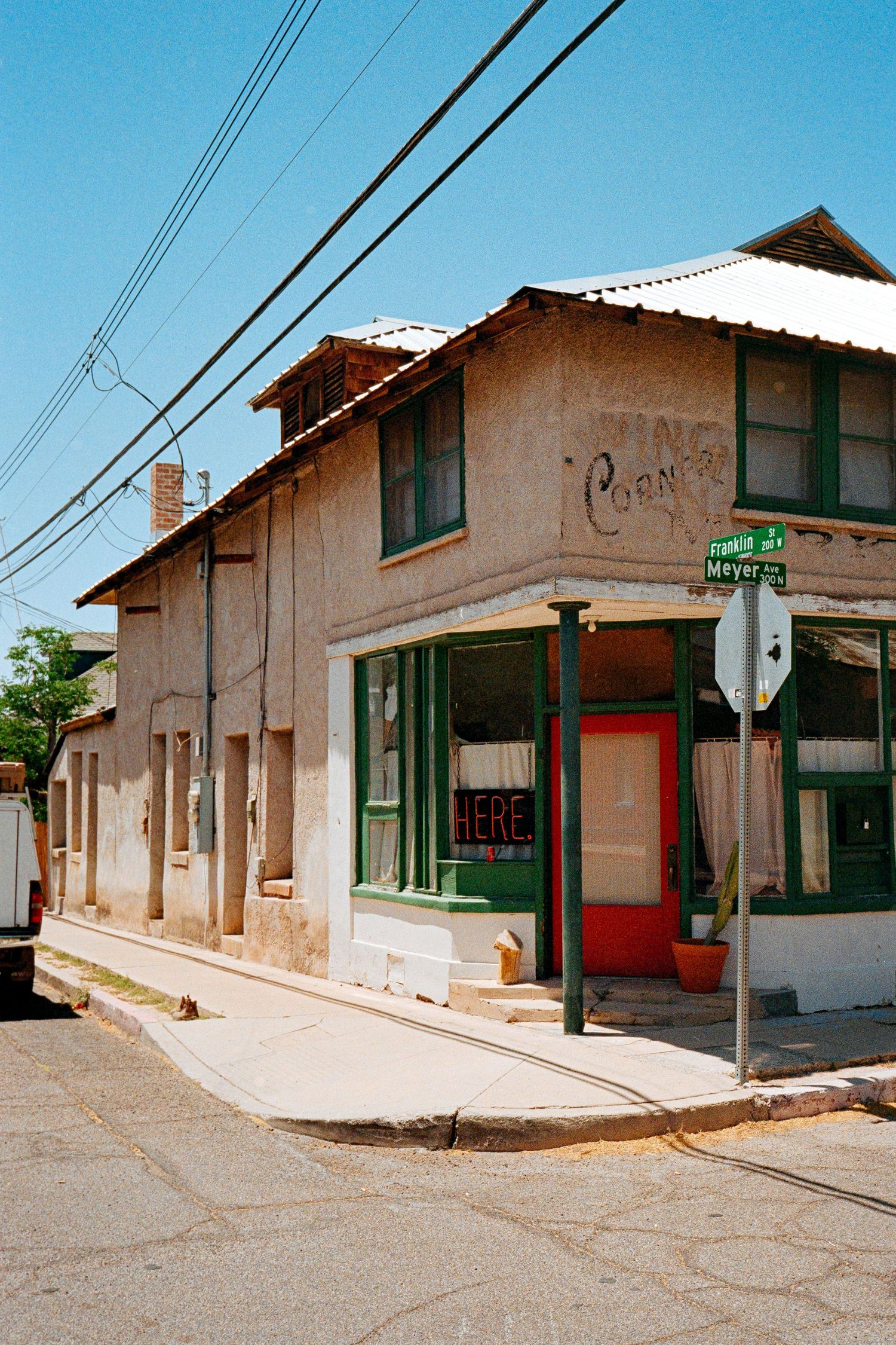 A vintage corner store building with green trim and red door on a sunny small-town street.
