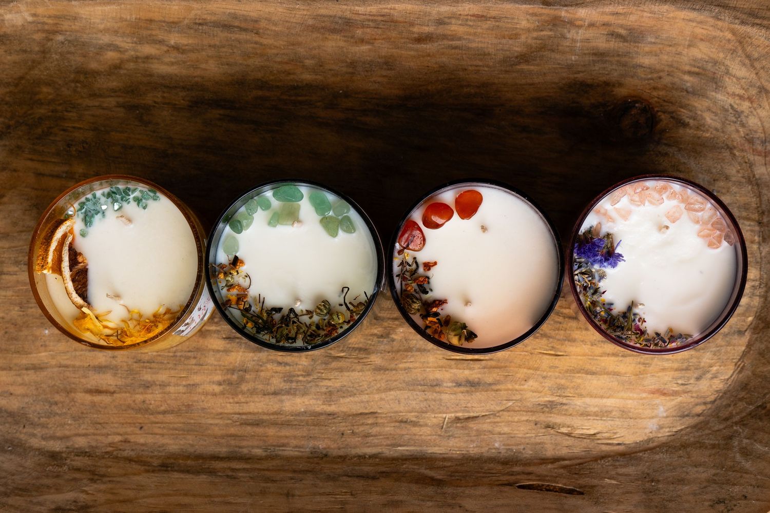Four small botanical soy wax candles with dried flowers viewed from above on wood surface.