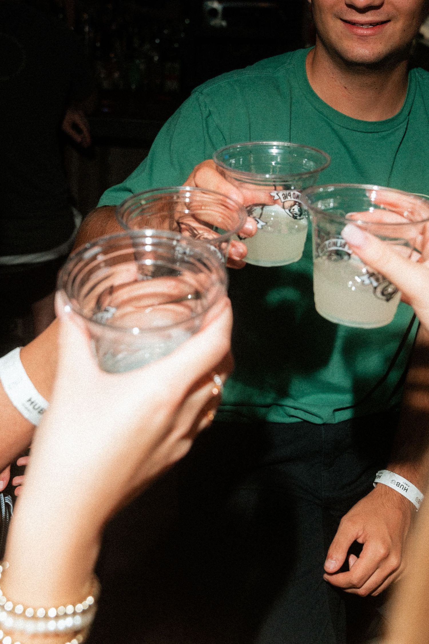 Group of friends toasting with cocktails at a party, wearing event wristbands.