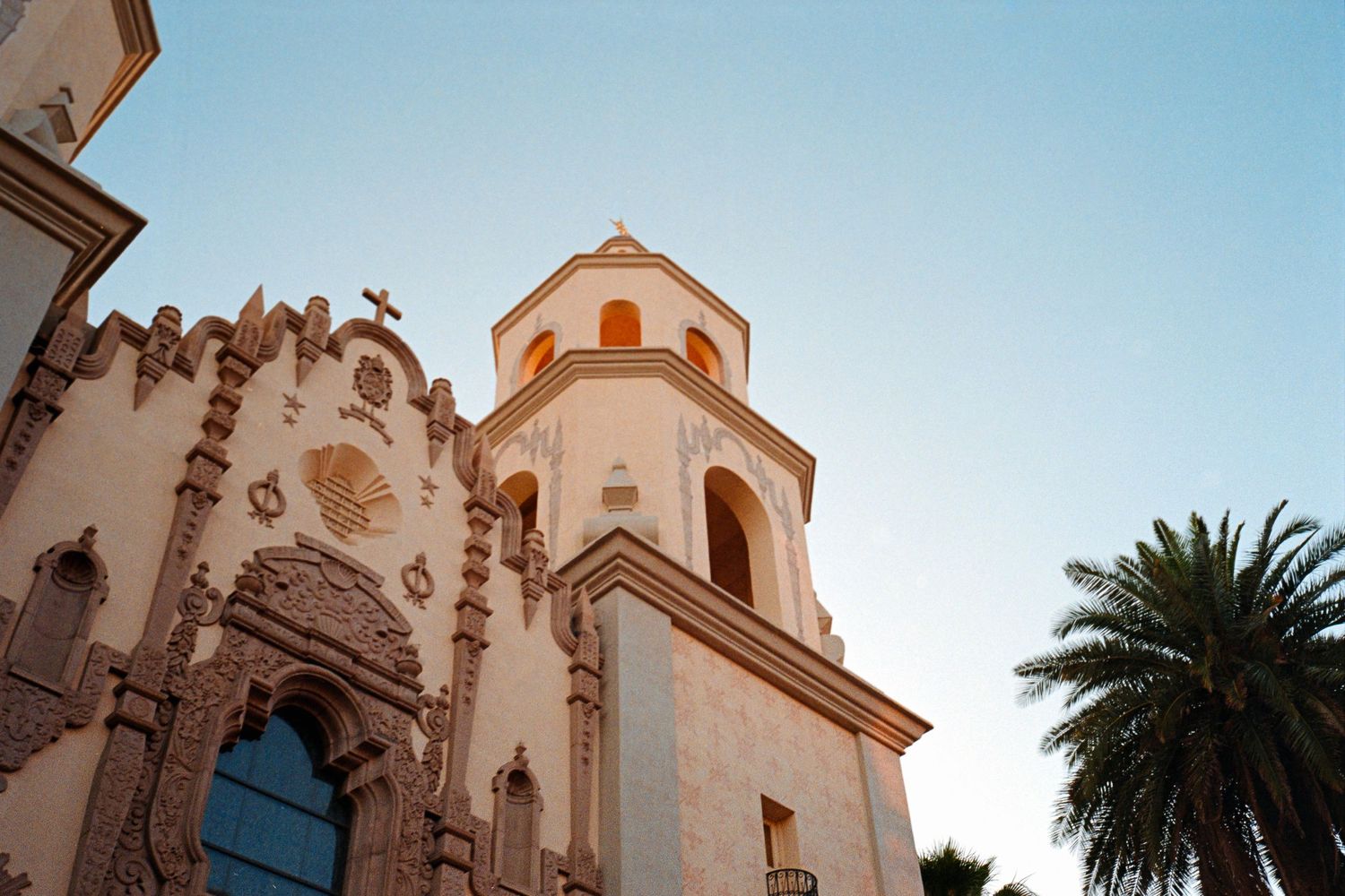 Low angle view of a Spanish colonial church tower against a clear blue sky with palm tree.