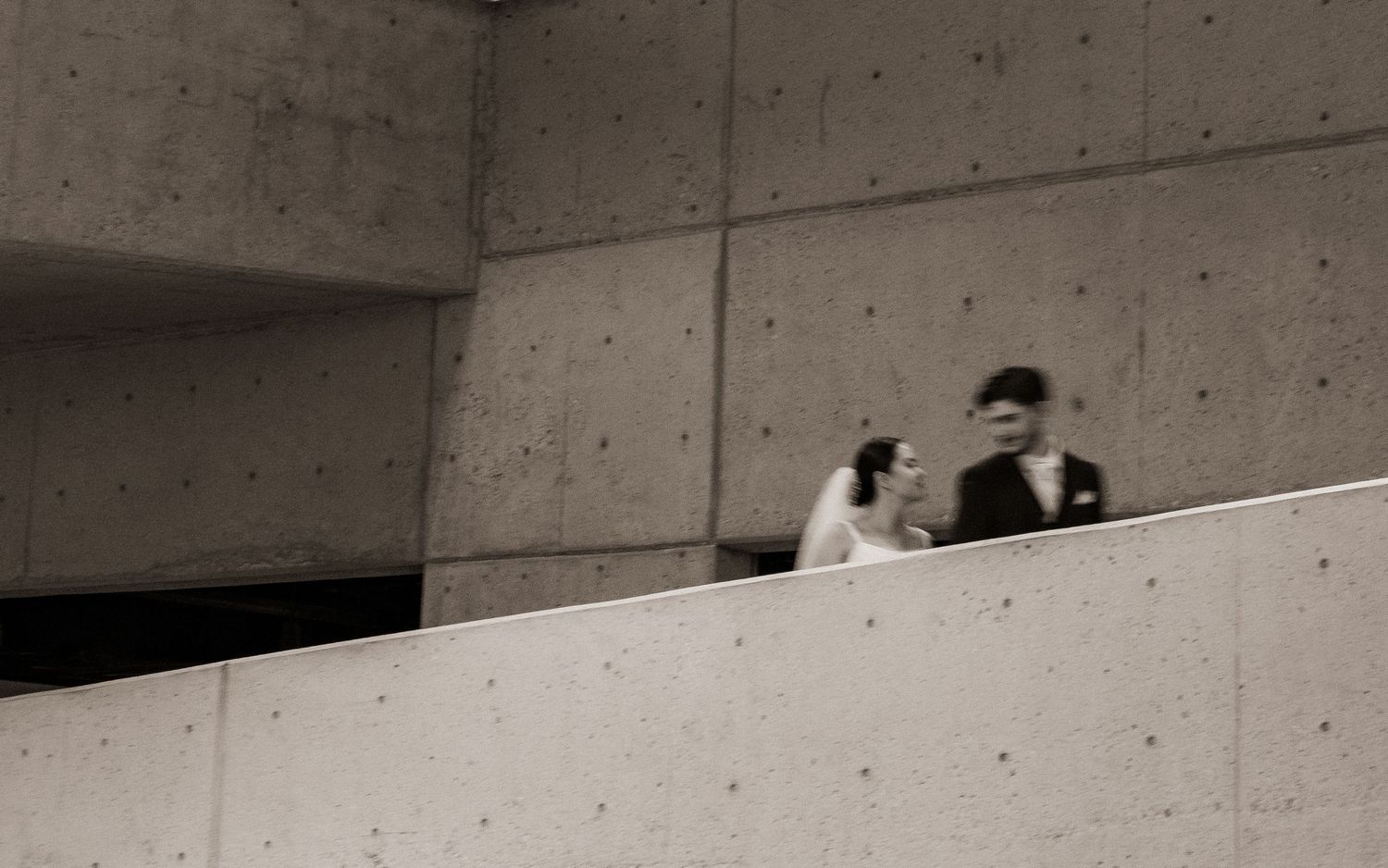 Bride and groom share a romantic moment on a concrete staircase in a modern architectural setting.