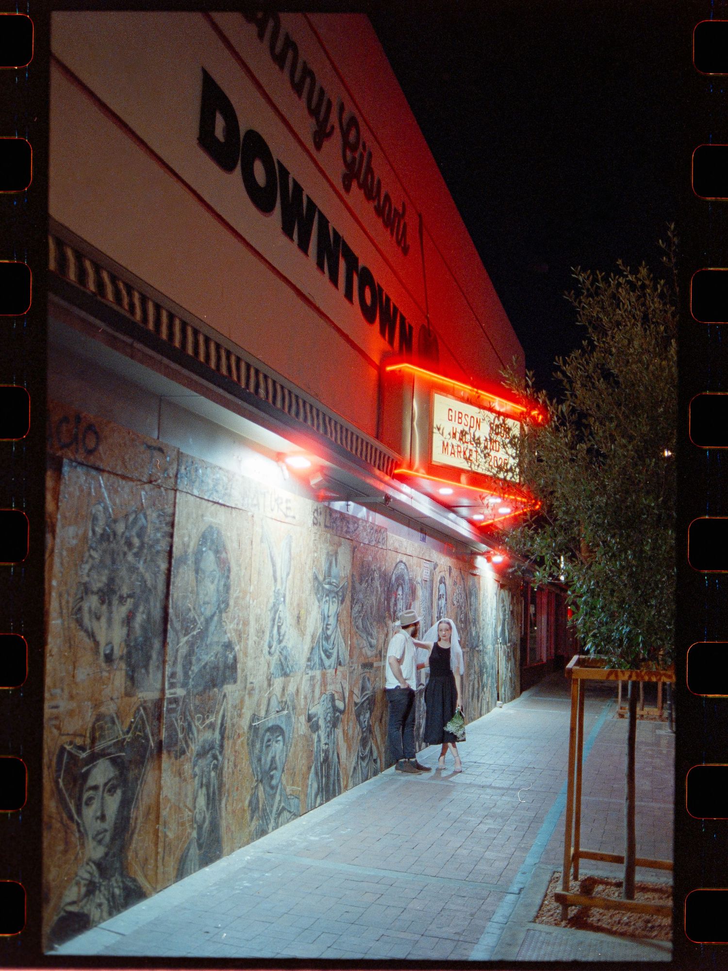Couple standing outside Downtown venue at night with neon lights and mural wall.