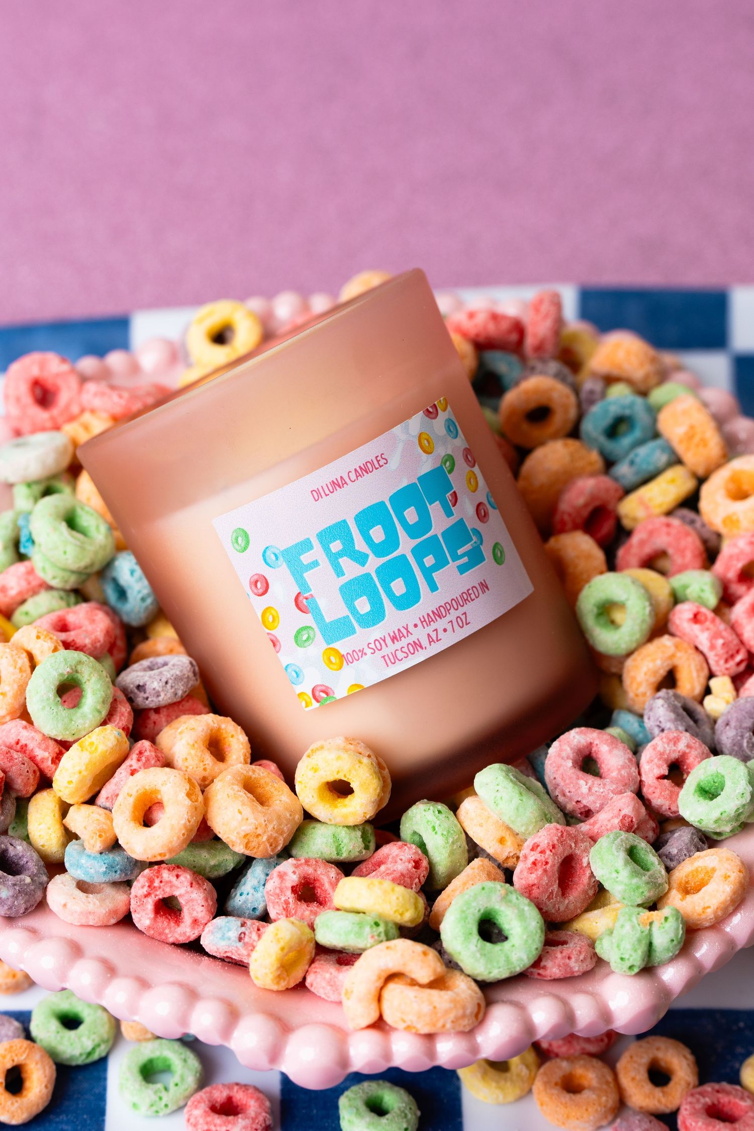 Di Luna Froot Loops scented candle surrounded by colorful cereal loops on pink plate.