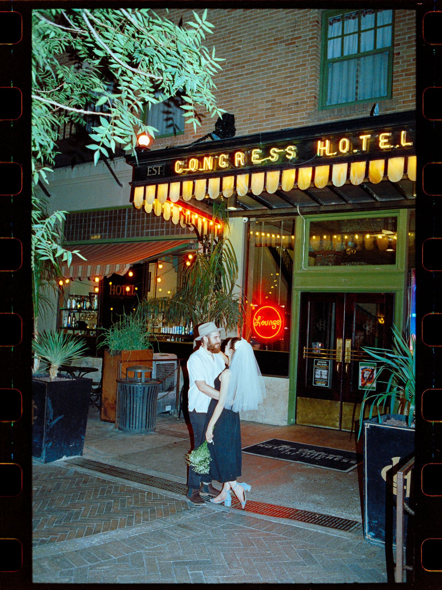 Wedding couple kissing outside the historic Congress Hotel with warm neon lights at night.