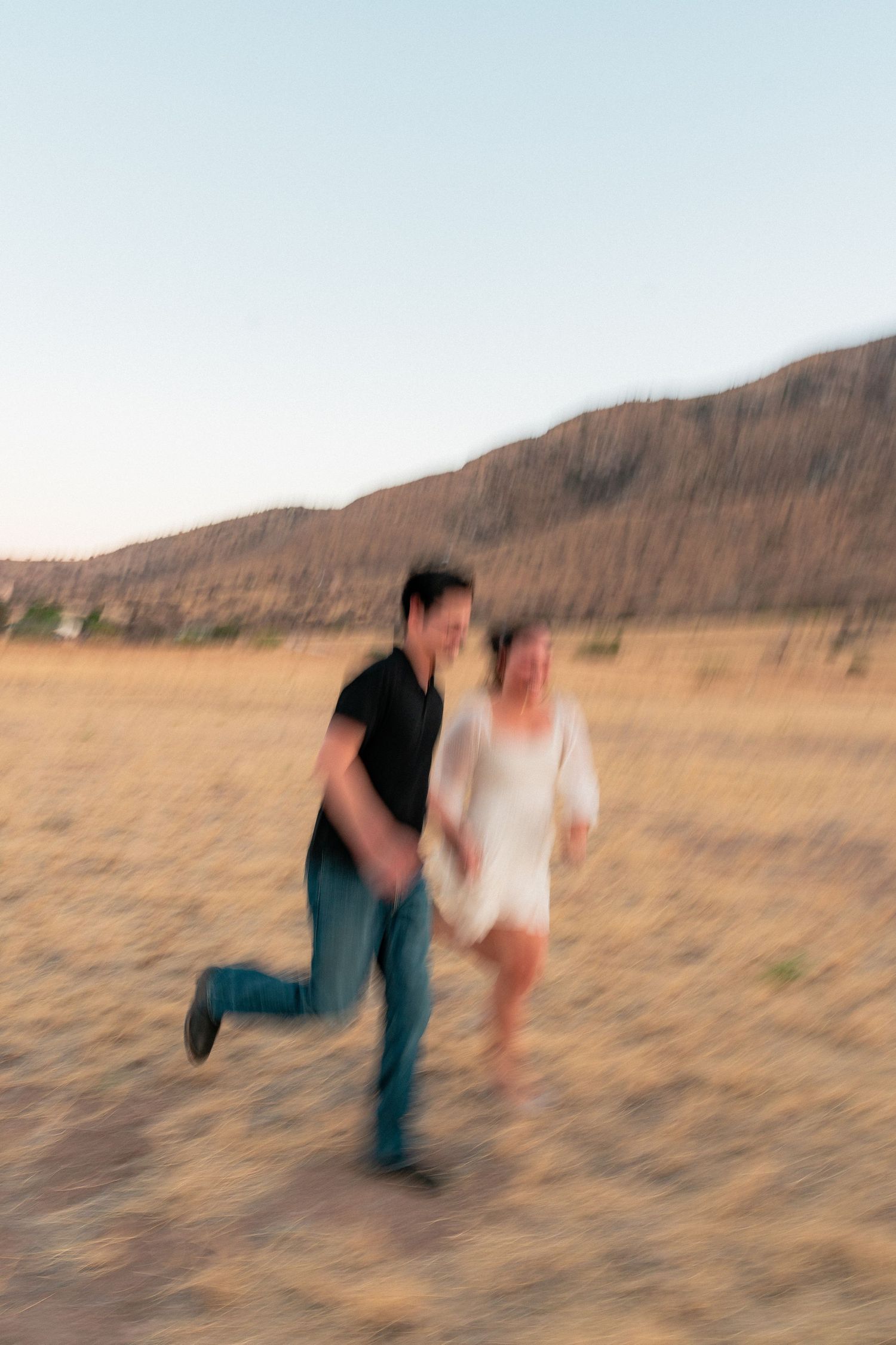 Blurred motion photo of a joyful couple running together in a golden desert field at dusk.