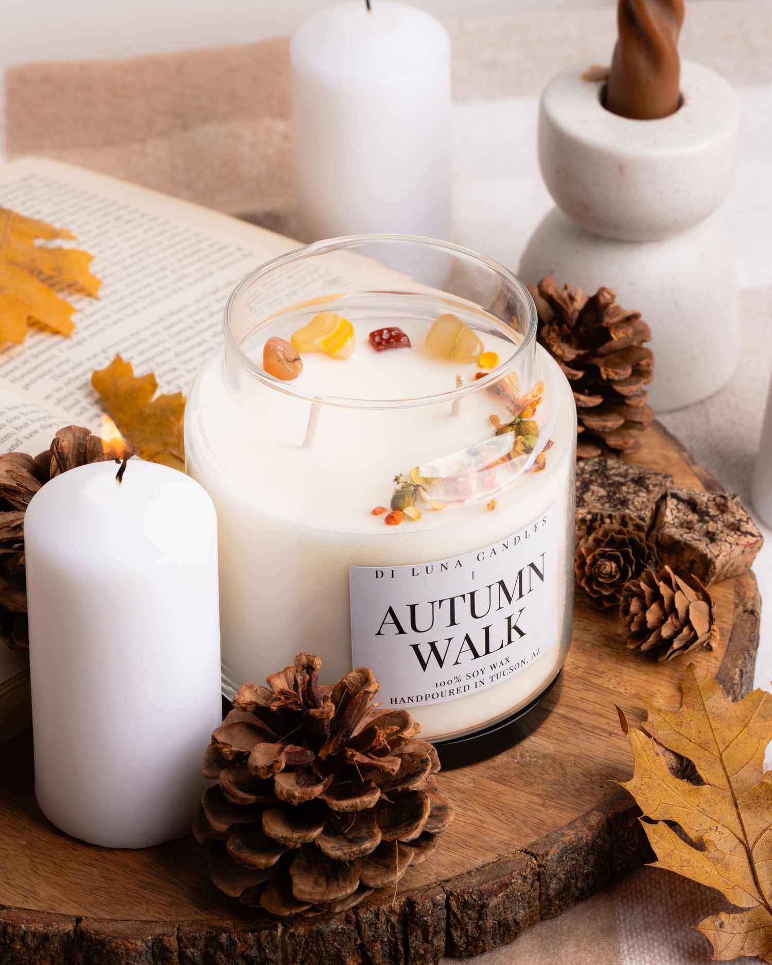 Di Luna Autumn Walk soy candle with dried botanicals surrounded by pine cones and fall leaves.