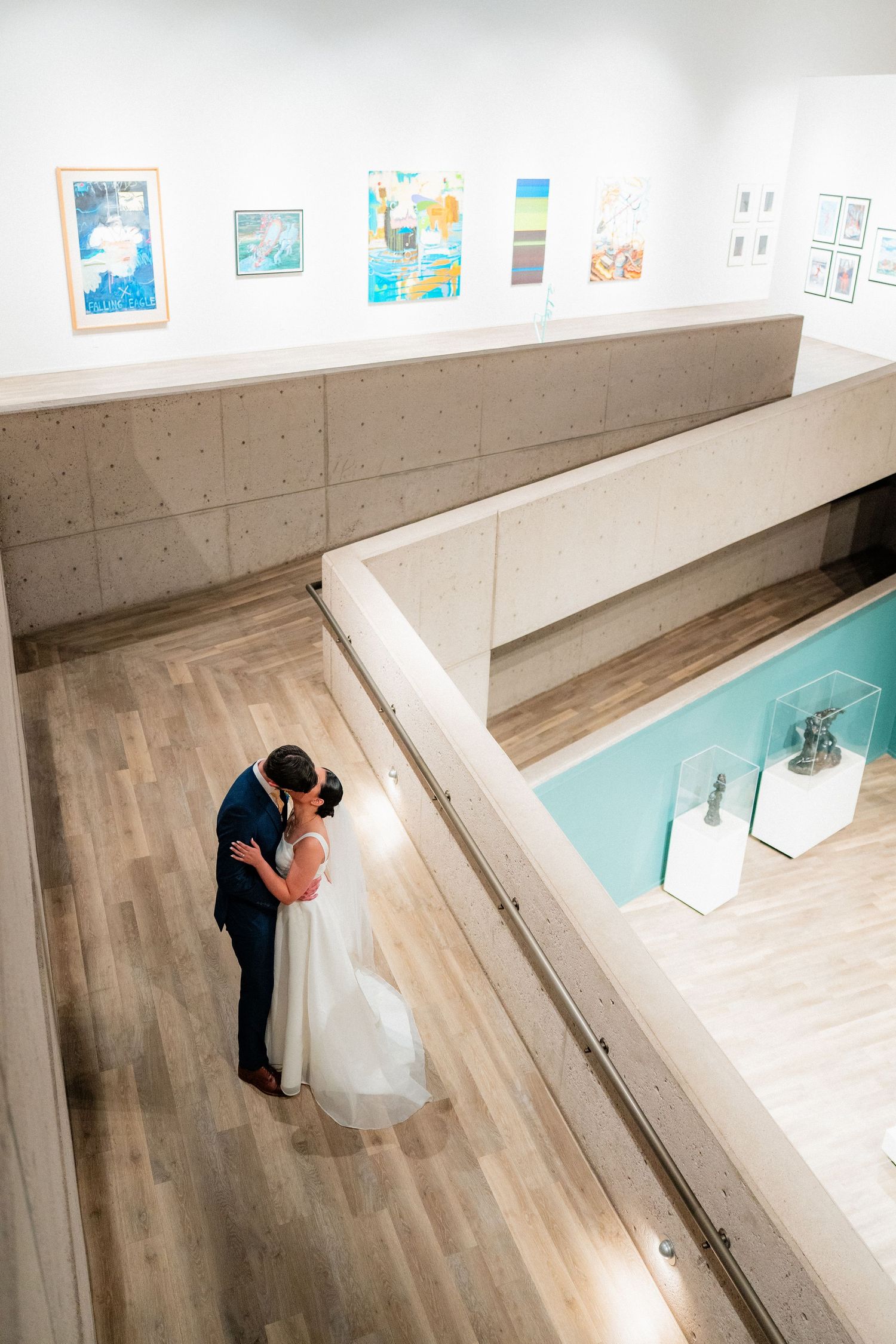 Aerial view of bride and groom embracing on wooden floor of modern art museum gallery on wedding day.