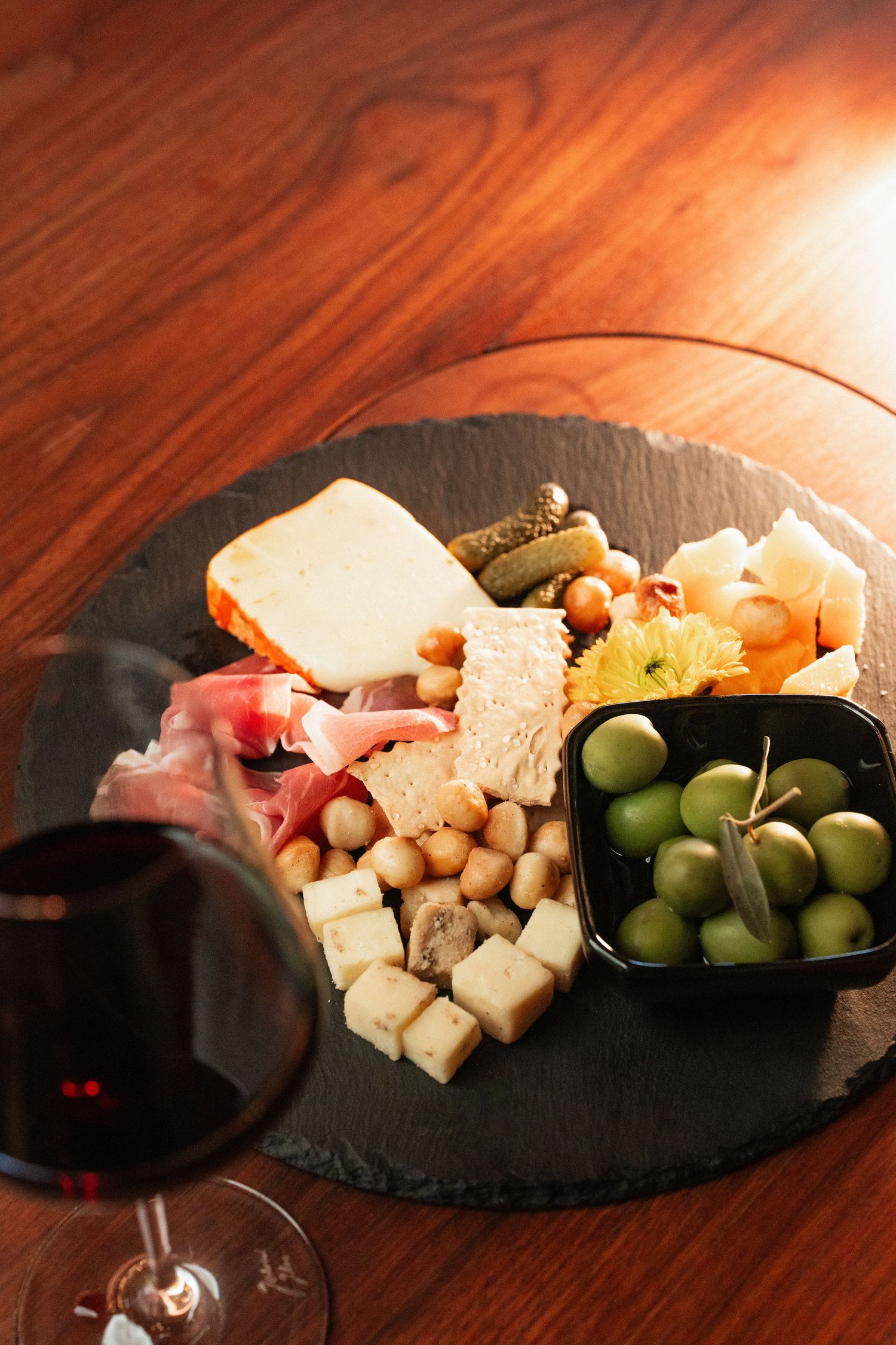 Charcuterie board with cheese, olives, prosciutto, and pickles served alongside a glass of red wine.