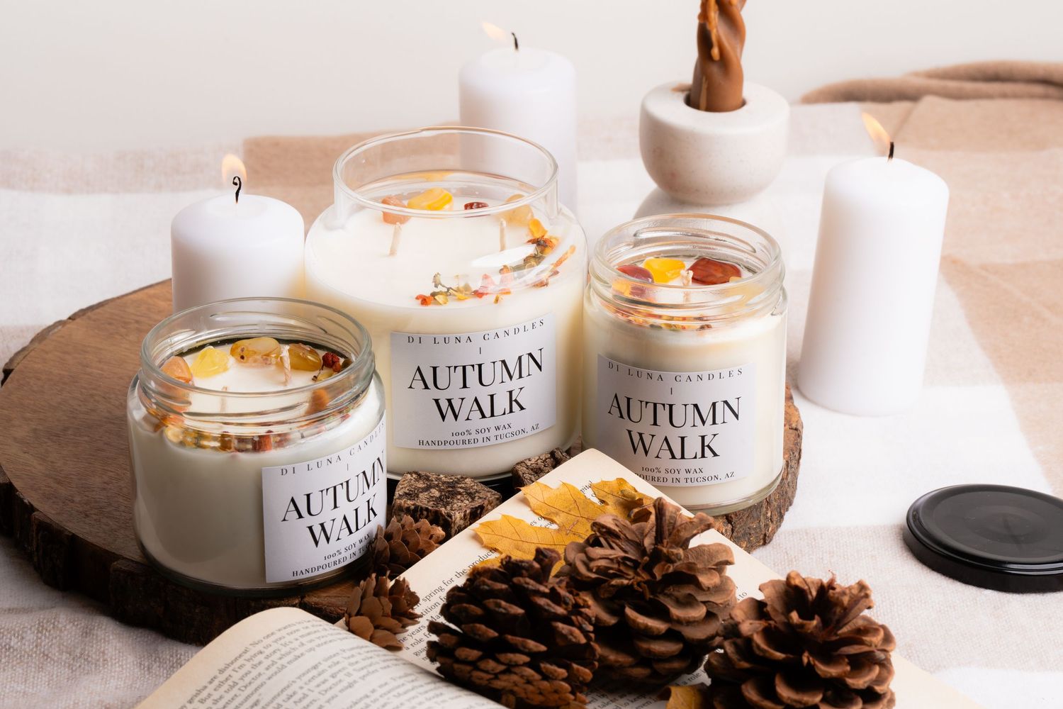 Three Di Luna Autumn Walk candles displayed on wood slice with pine cones and open book.