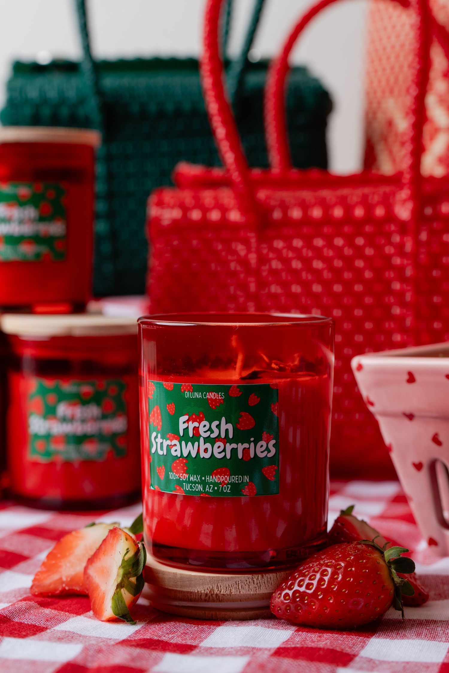 Fresh Strawberries scented red glass candle on red gingham tablecloth with real strawberries.