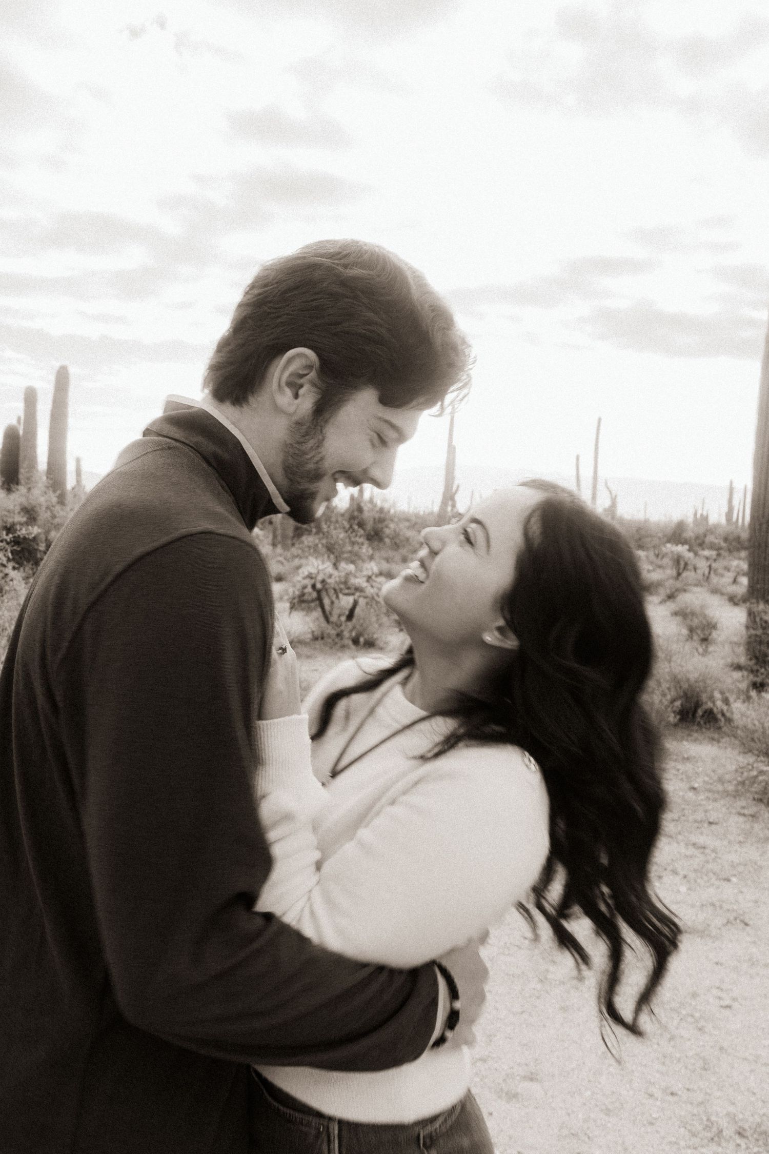 Black and white photo of a couple nearly kissing surrounded by desert cacti.