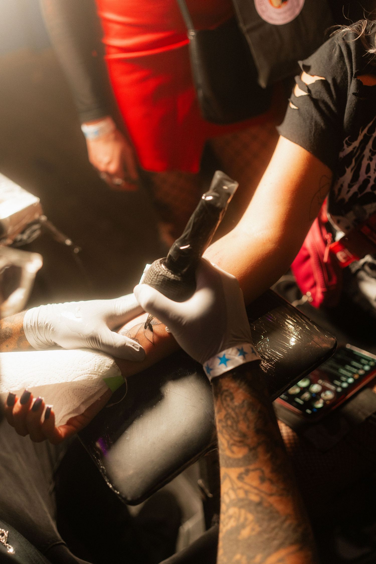 Tattoo artist in white gloves applying tattoo on clients foot under warm studio lighting.