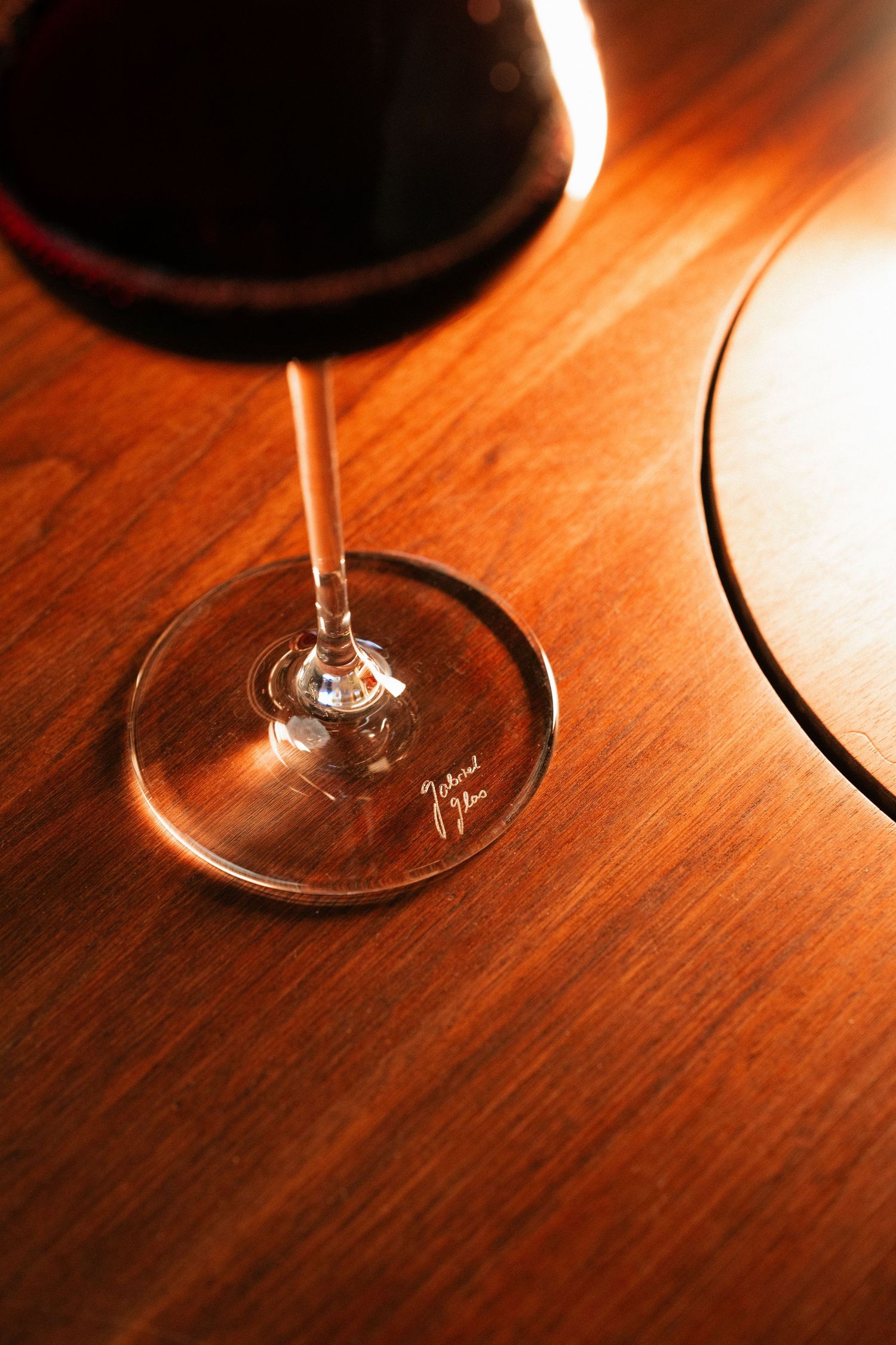 Close-up of a red wine glass on a warm wooden table with soft sunlight highlighting the stem.