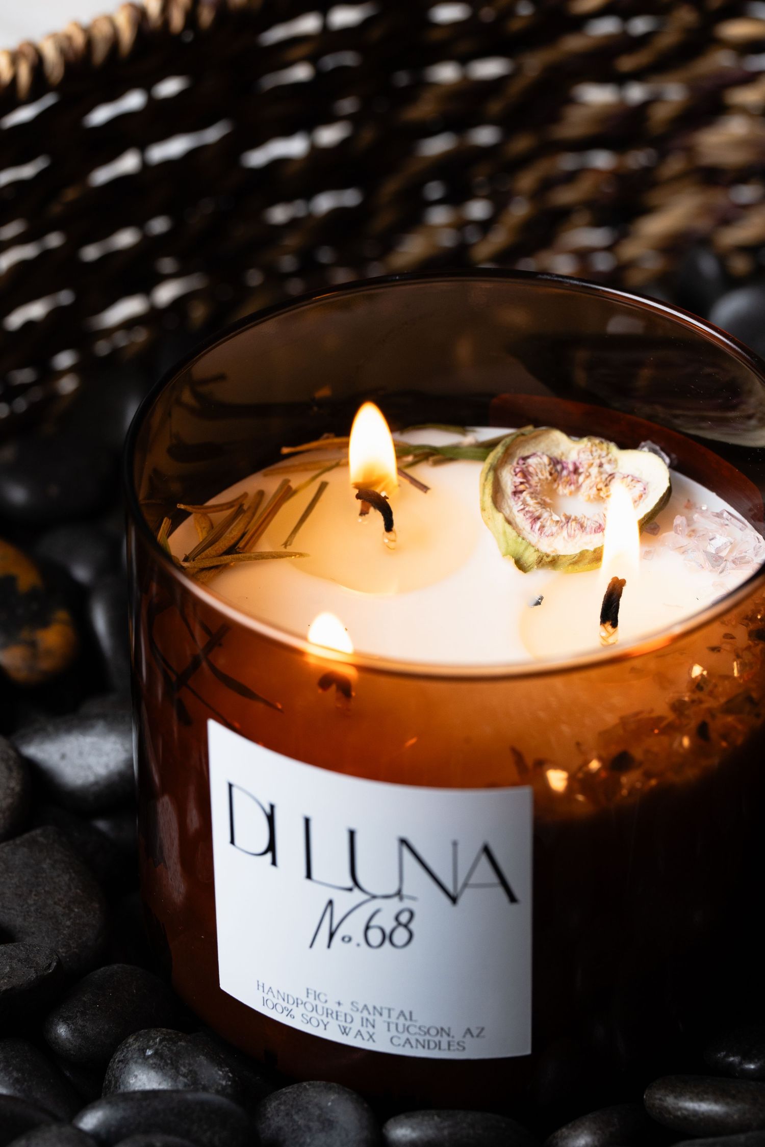 Di Luna No.68 Fig and Santal scented candle burning in amber glass jar on black stones.