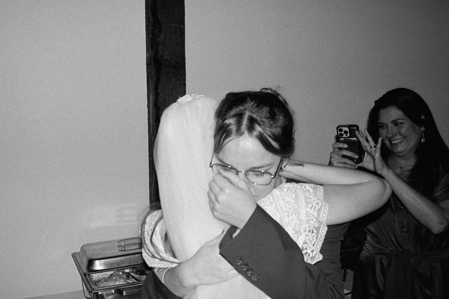 Black and white photo of emotional bride being comforted with a hug at wedding reception.