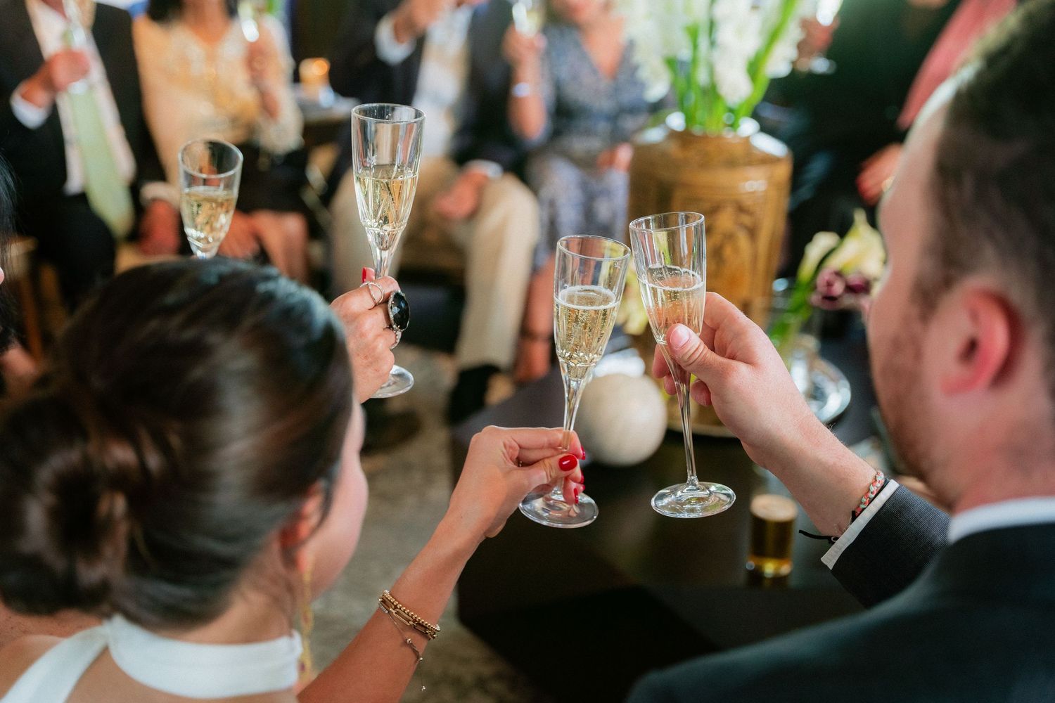 Bride and groom clink champagne flutes with guests during a festive wedding reception toast.