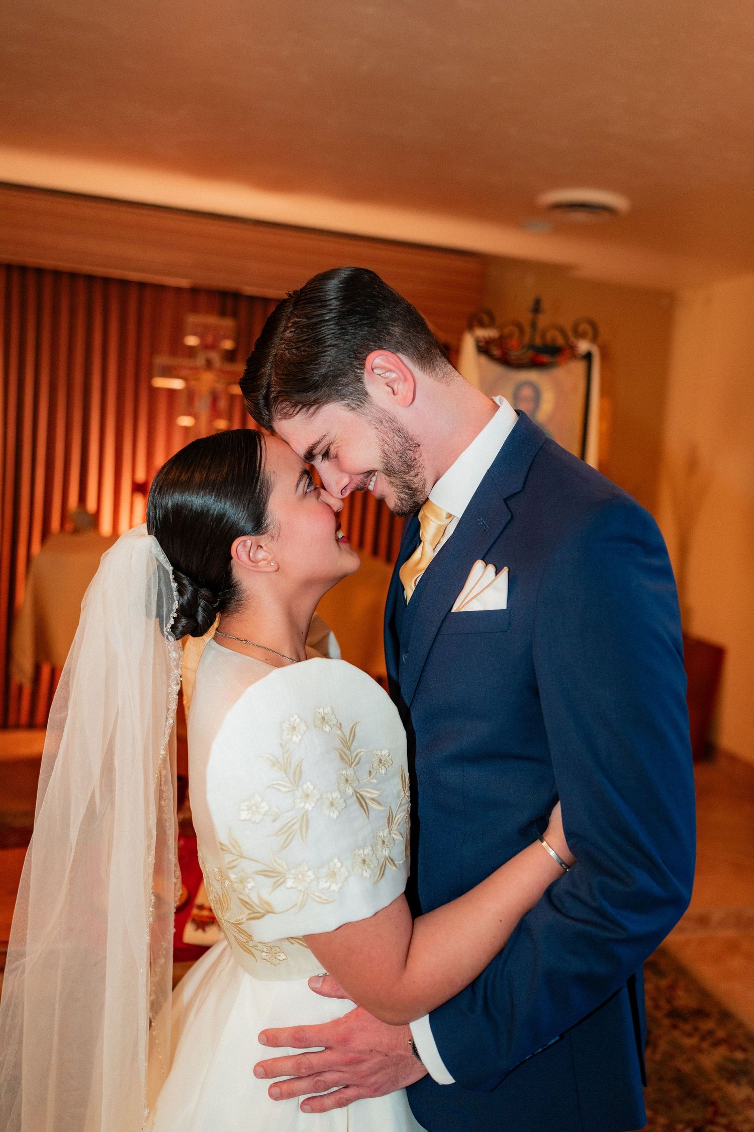 Bride and groom sharing an intimate moment, nearly kissing, in warm indoor light at their wedding.