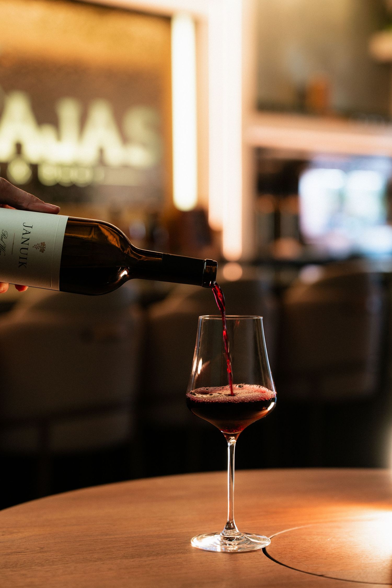Red wine being poured from a bottle into an elegant glass at Tinajas Wine and Beer bar.