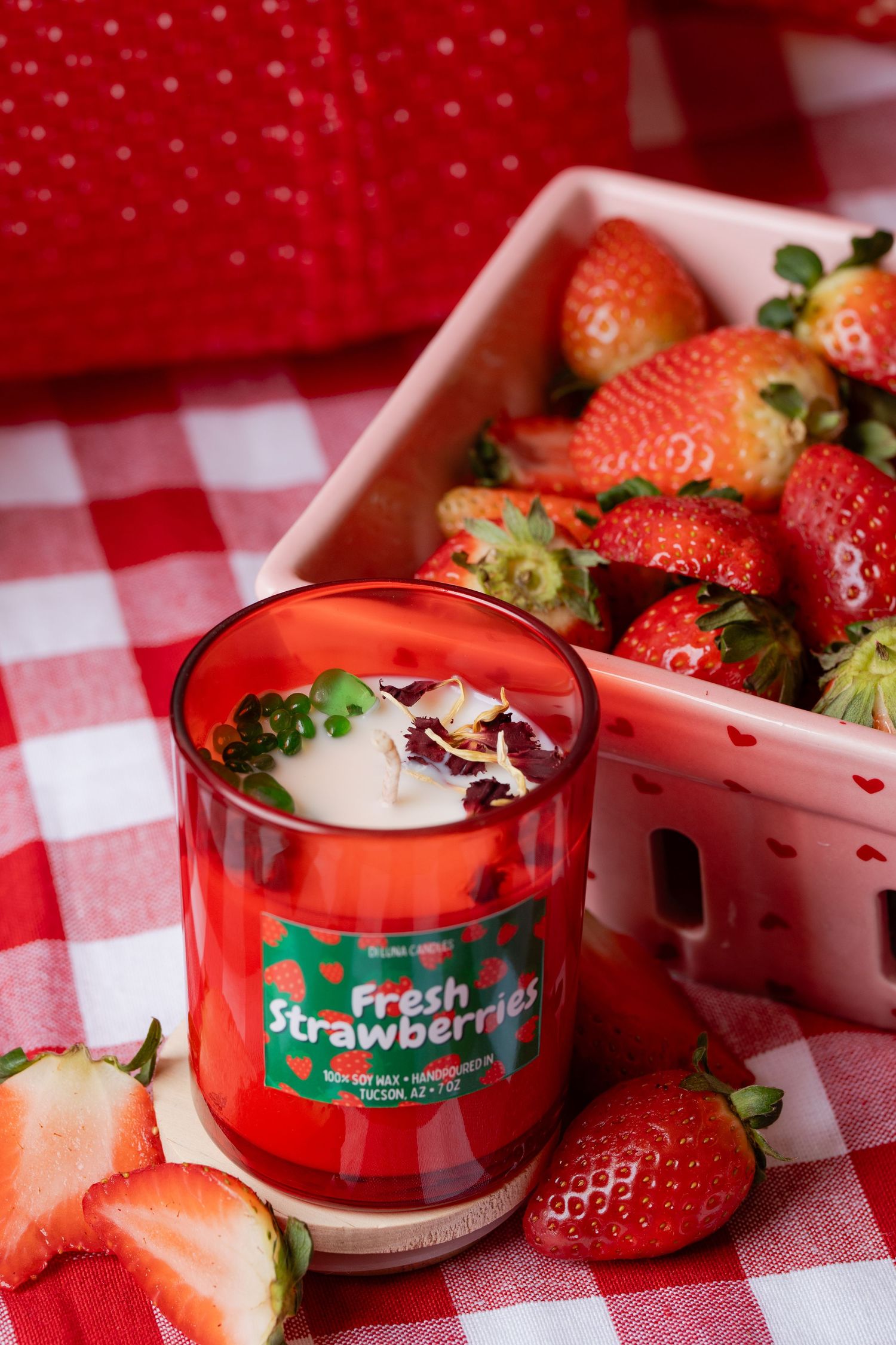 Fresh Strawberries Di Luna candle beside a white berry basket filled with ripe strawberries.