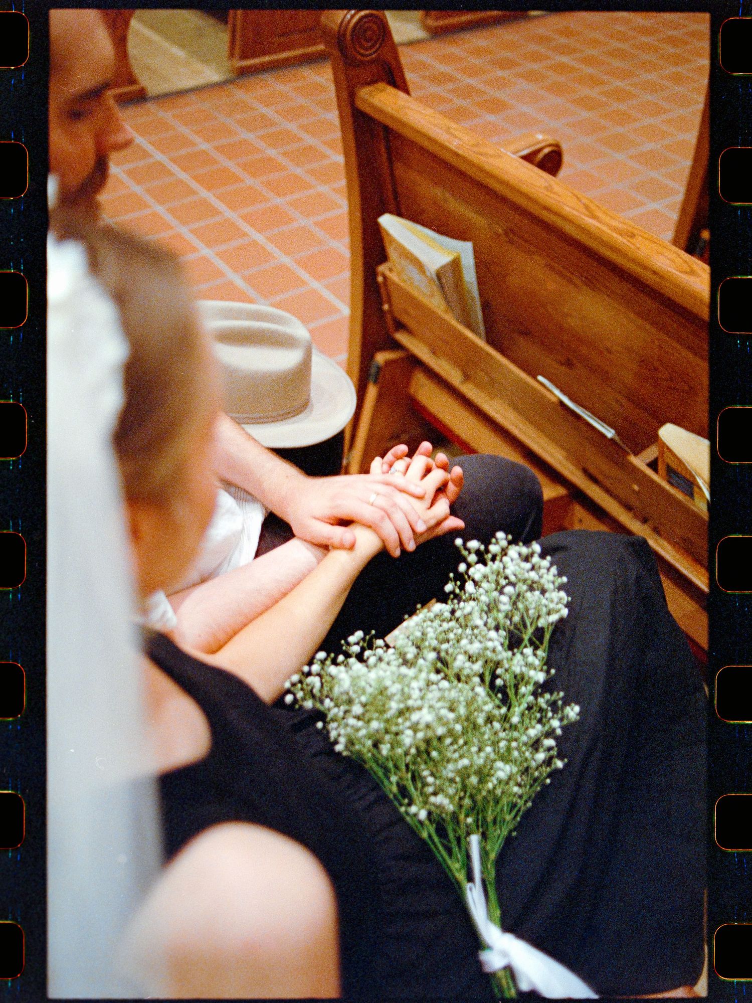 Film photo of wedding guests holding hands in church pew beside a baby's breath bouquet.