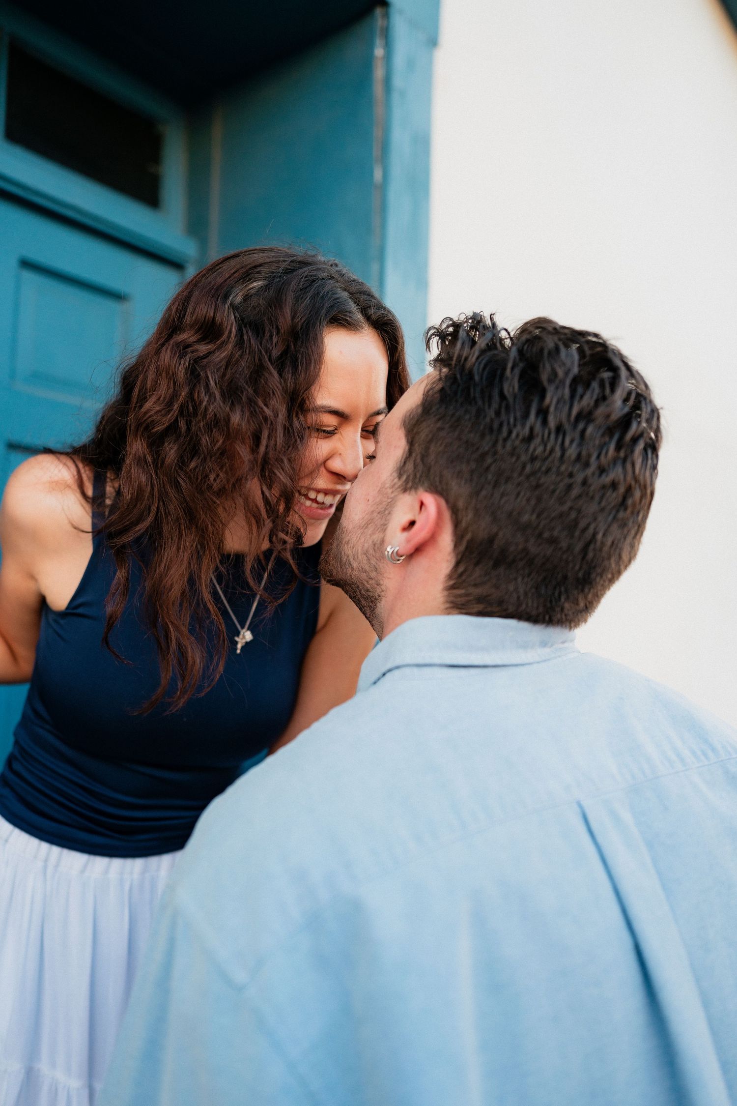 Happy couple sharing an intimate moment near a blue door during their engagement session.