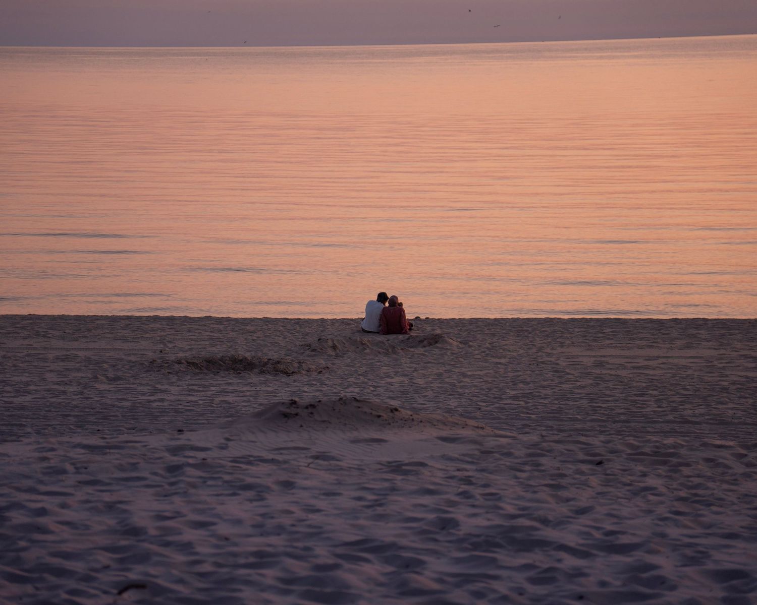 Silhouettes on beach at sunset with pink and orange sky reflection on water.
