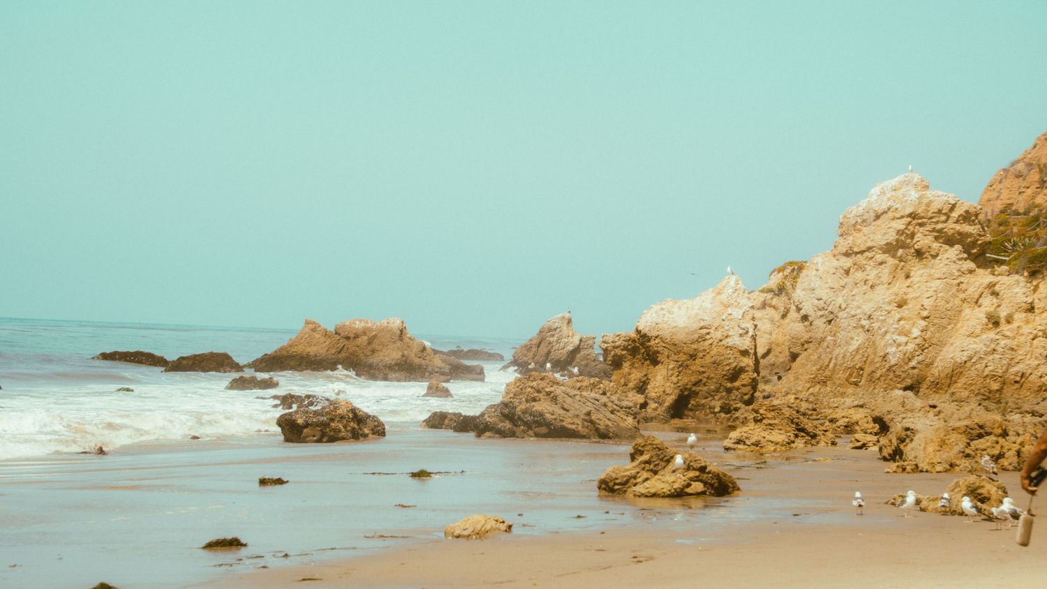 Sandy beach dotted with rock formations along weathered coastal cliffs.