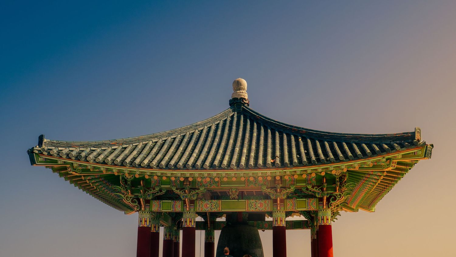 Detailed view of traditional Korean pavilion roof against gradient sky.
