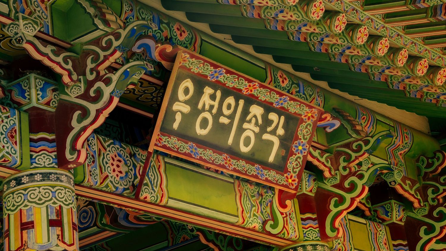 Close-up of Korean temple woodwork showing painted decorative patterns and Korean text.