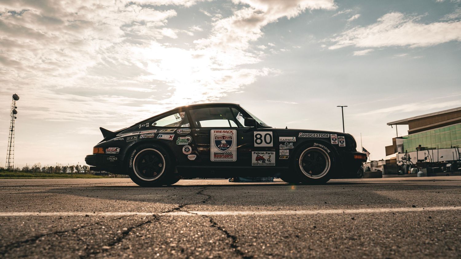Vintage Porsche 911 race car with number 80 captured against dramatic cloudy sky.