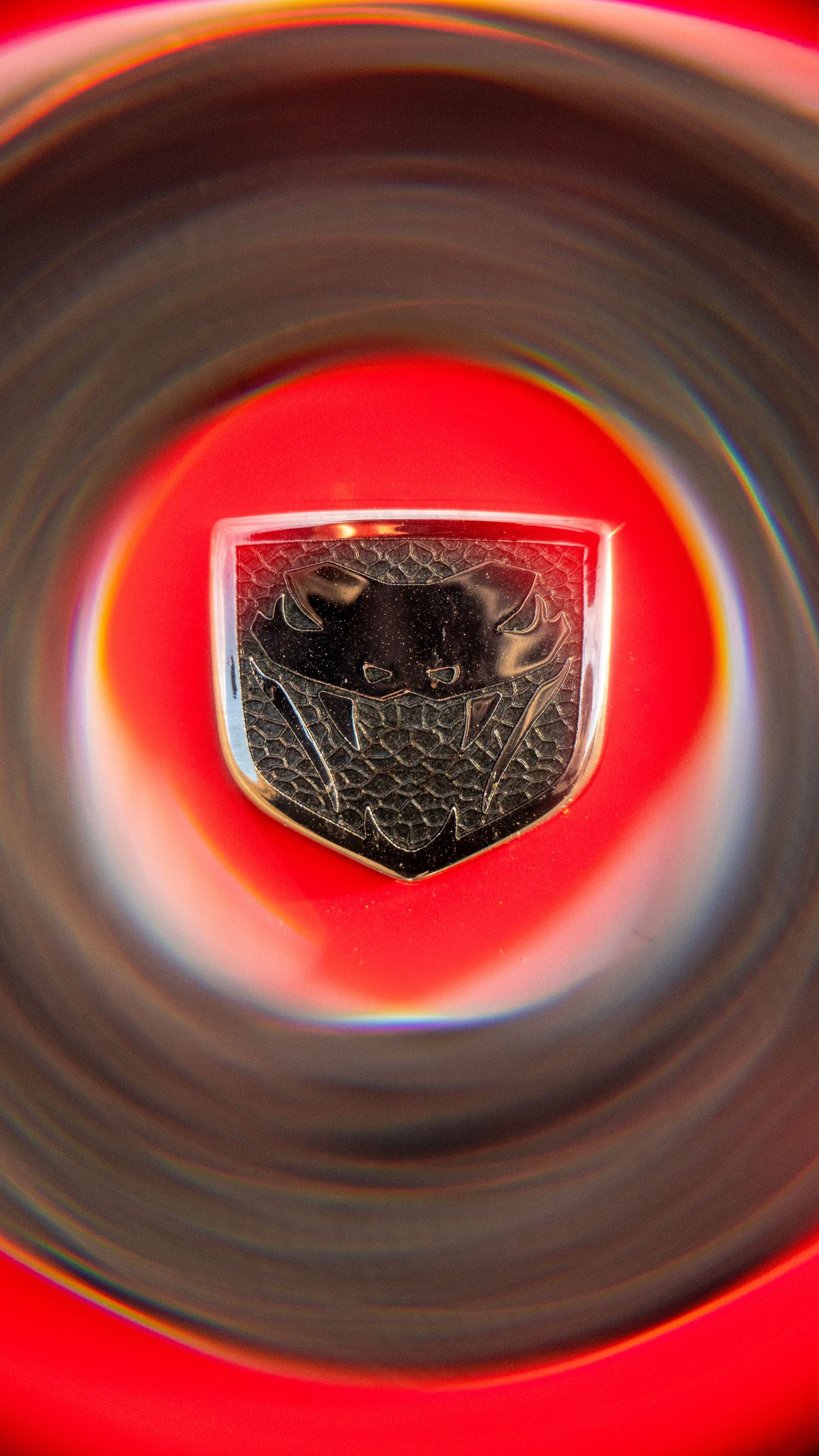 Close-up of a Dodge emblem badge against red background with circular vignette effect.