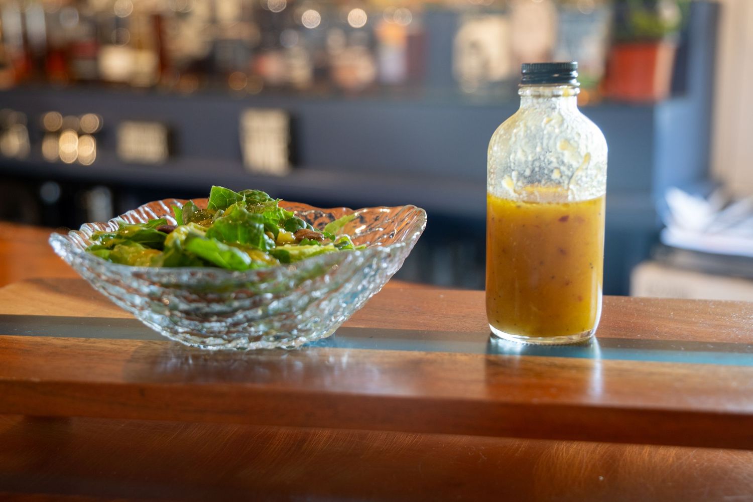 Fresh garden salad in crystal bowl served with yellow dressing in glass bottle.