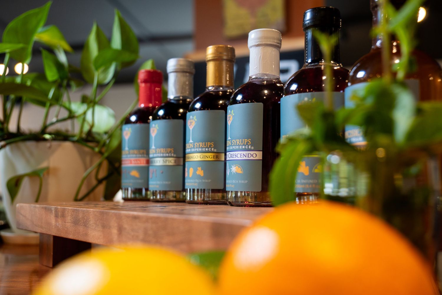Row of dark glass bottles with blue labels displayed against green plants and oranges.