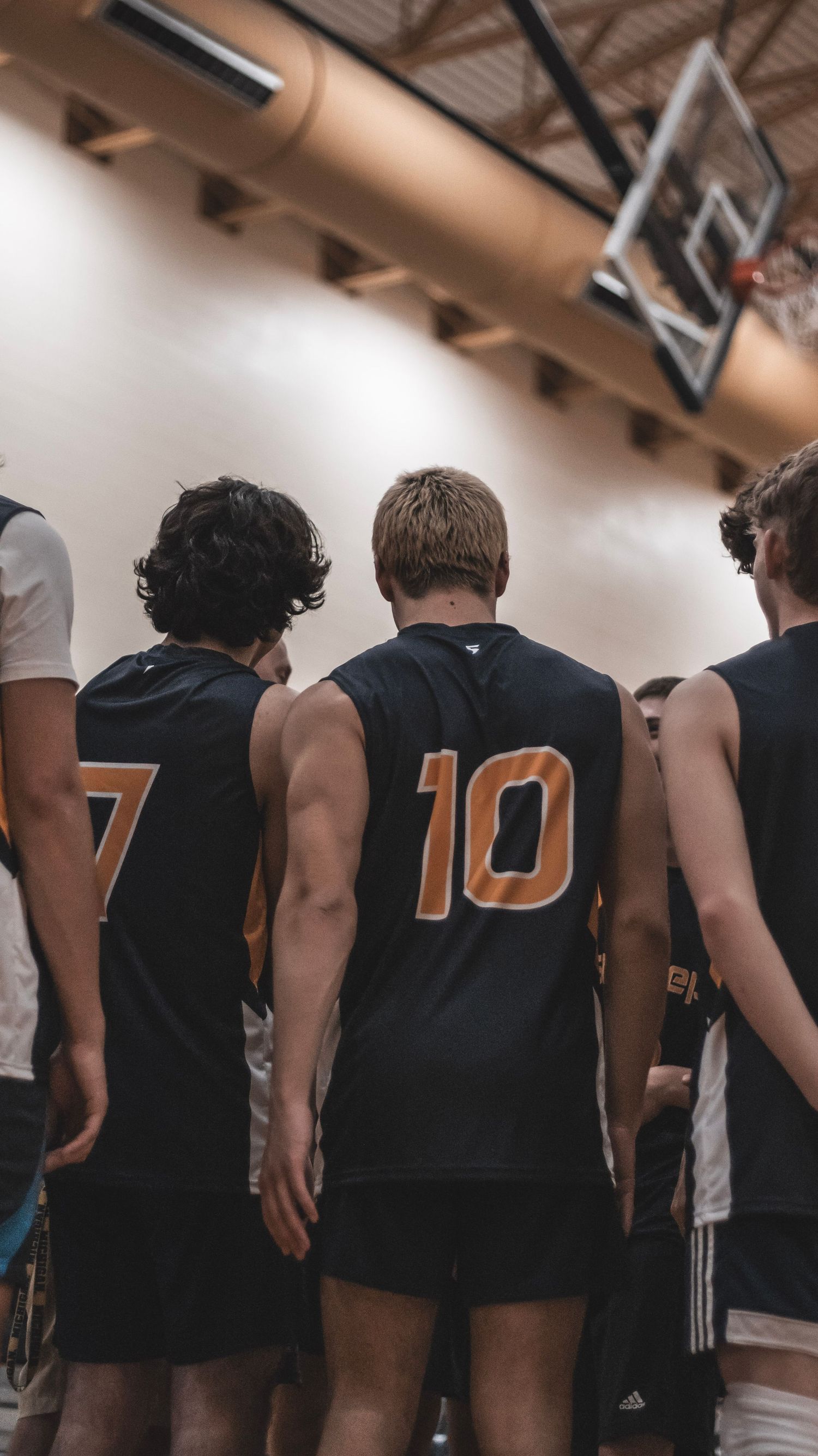 Basketball players in black jerseys stand together on court showing uniform numbers during game.