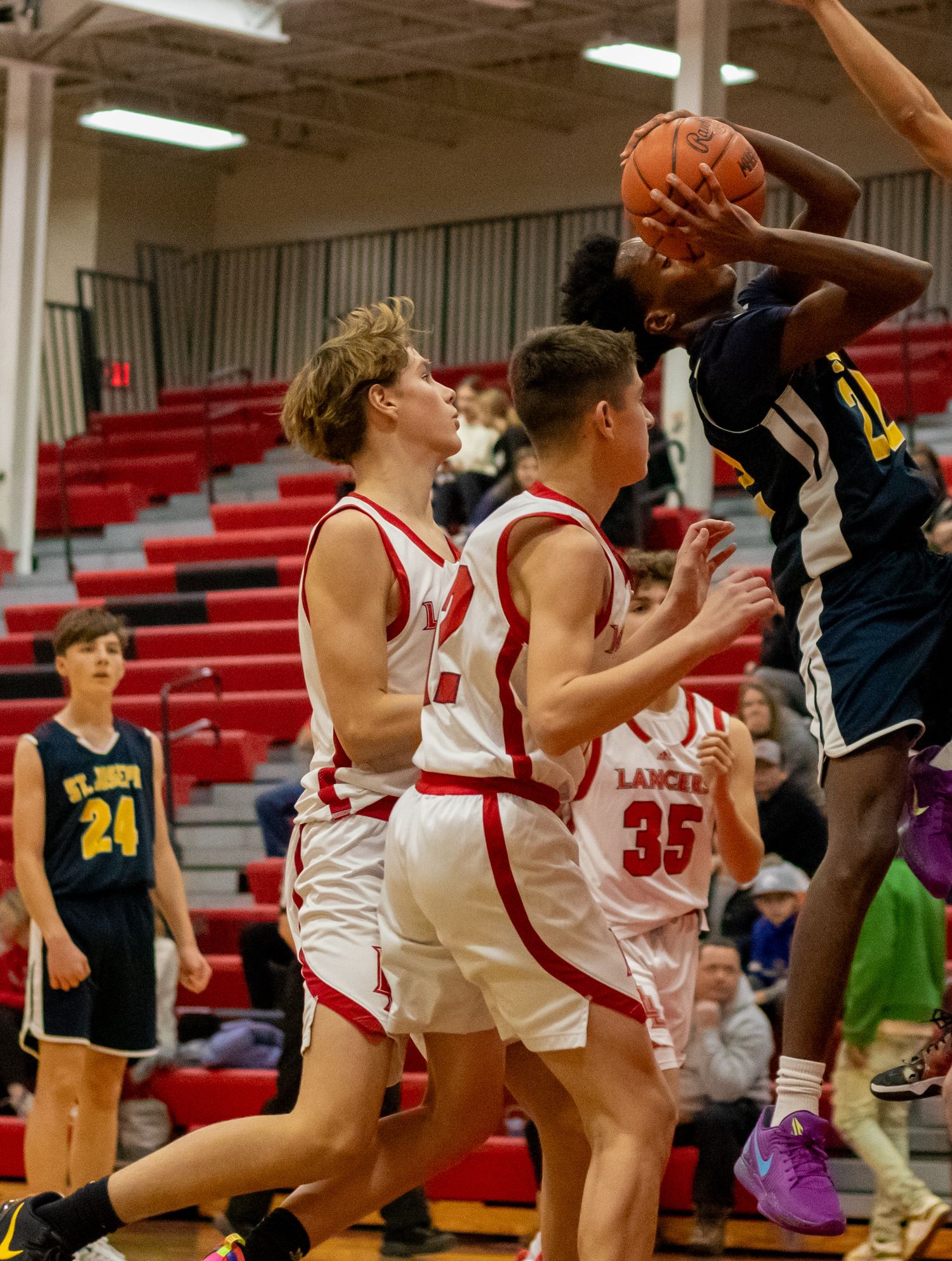 Basketball teams in navy and white uniforms compete for possession during an indoor game.