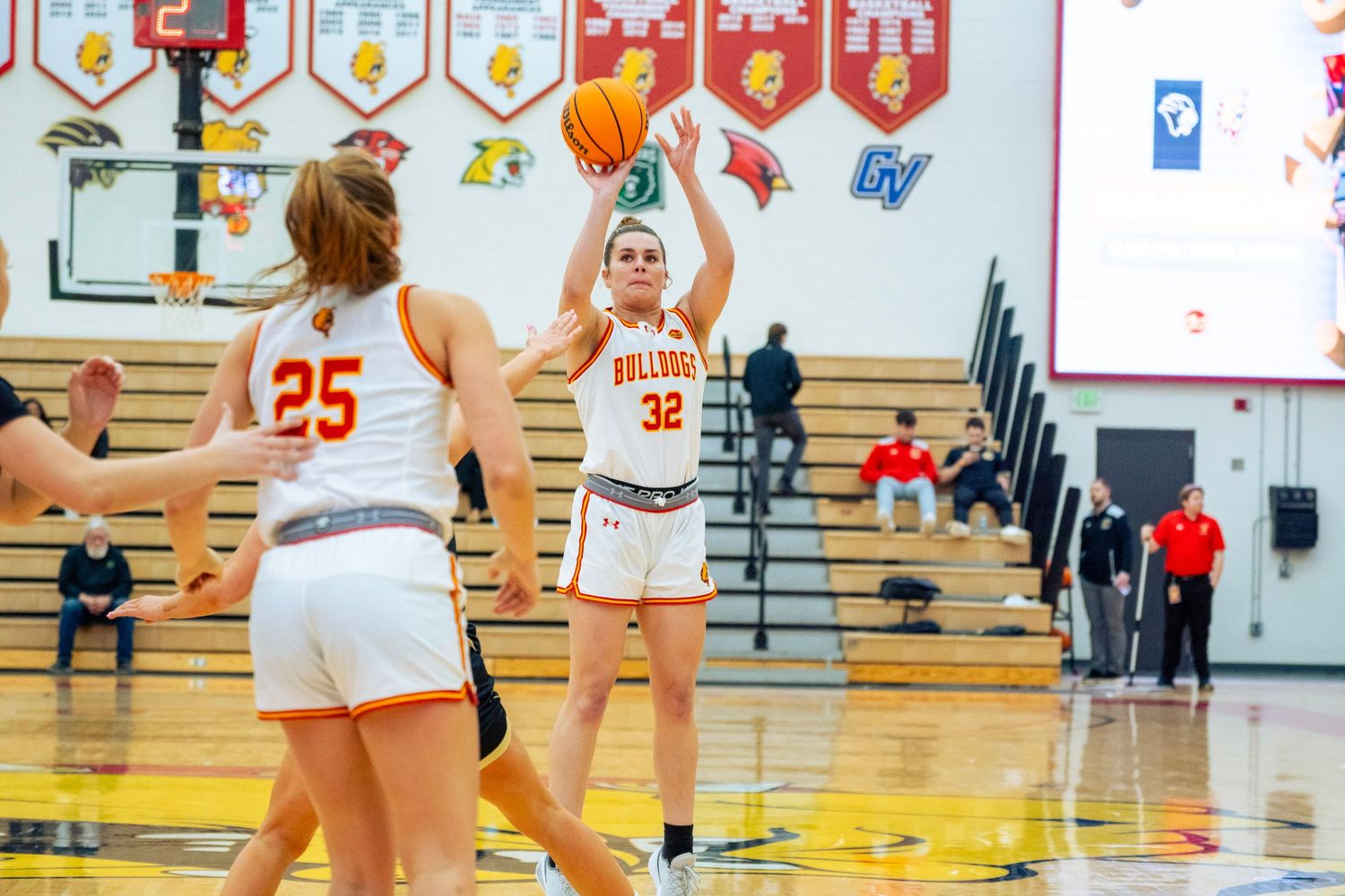 Basketball players in white uniforms compete during a high school game in a gymnasium.