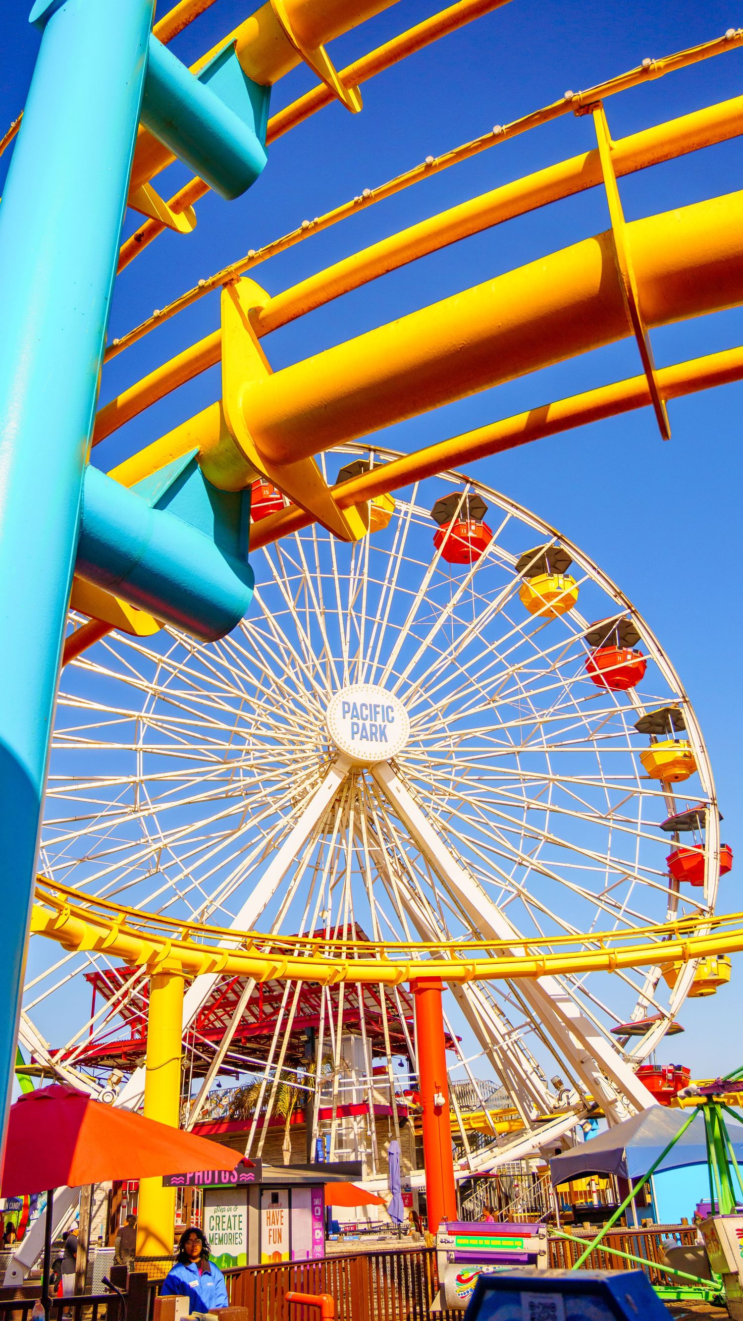 Low angle view of amusement park rides featuring bright turquoise supports and yellow beams against blue sky.