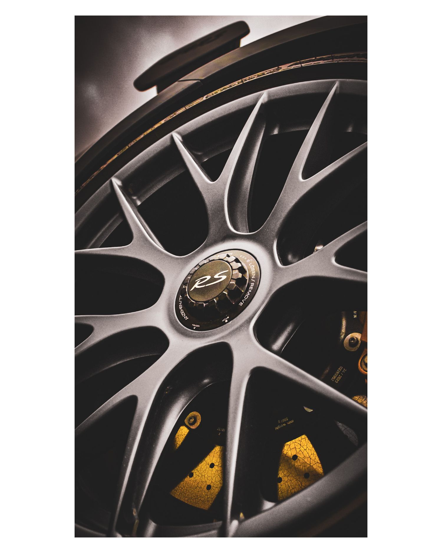 Detail shot of silver multi-spoke sports car wheel with yellow brake caliper visible behind.