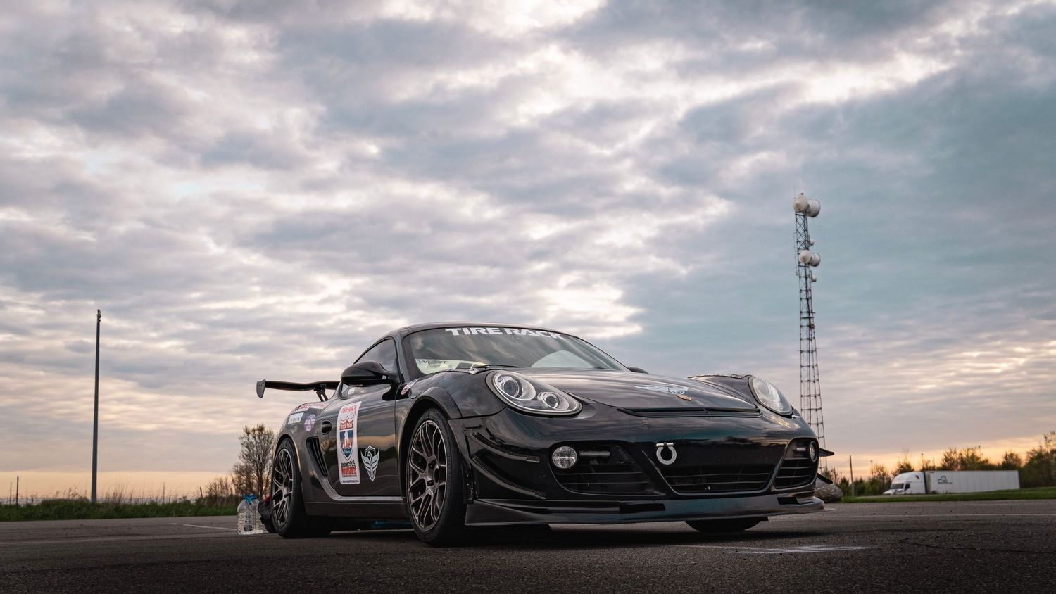 Modified sports car with racing aerodynamics photographed at sunset against cloudy sky.