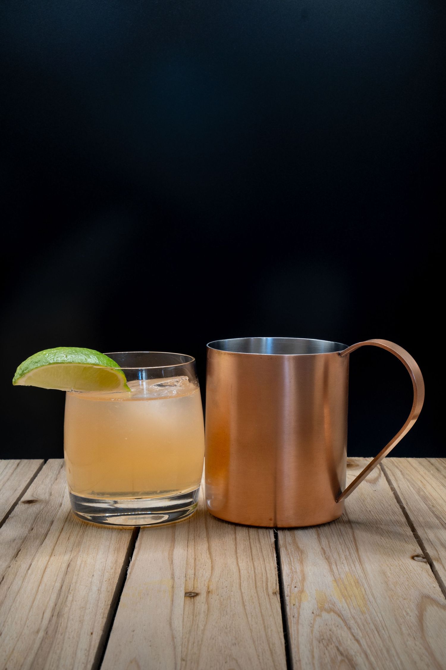 Moscow mule cocktail with lime and copper mug on weathered wood planks.