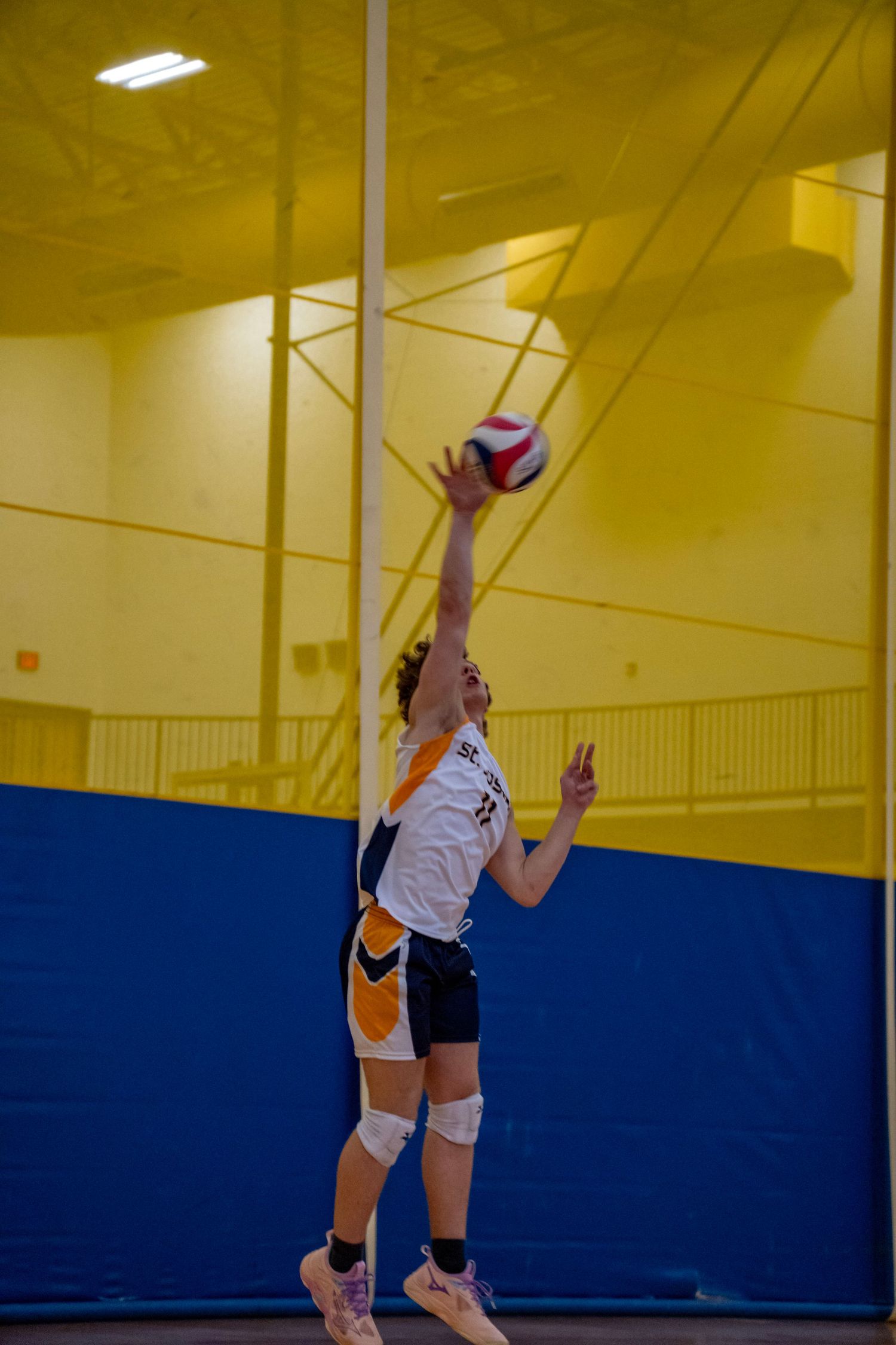 Player in white uniform jumping to hit volleyball during competitive indoor match.