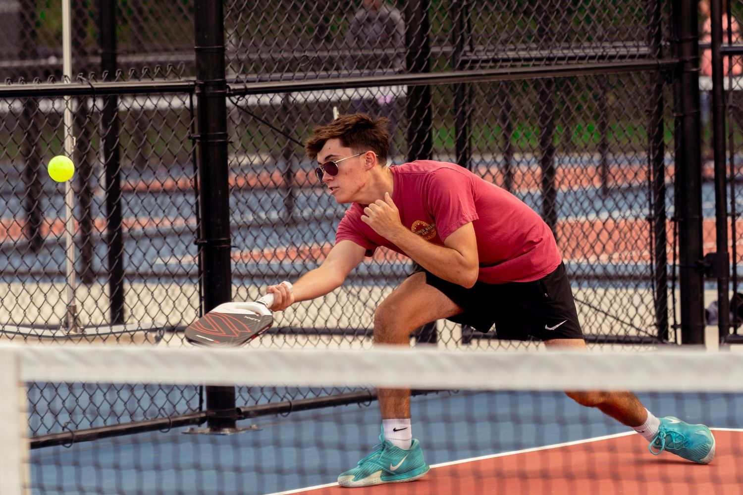 Tennis player stretches to return a serve during an outdoor match on a sunny day.