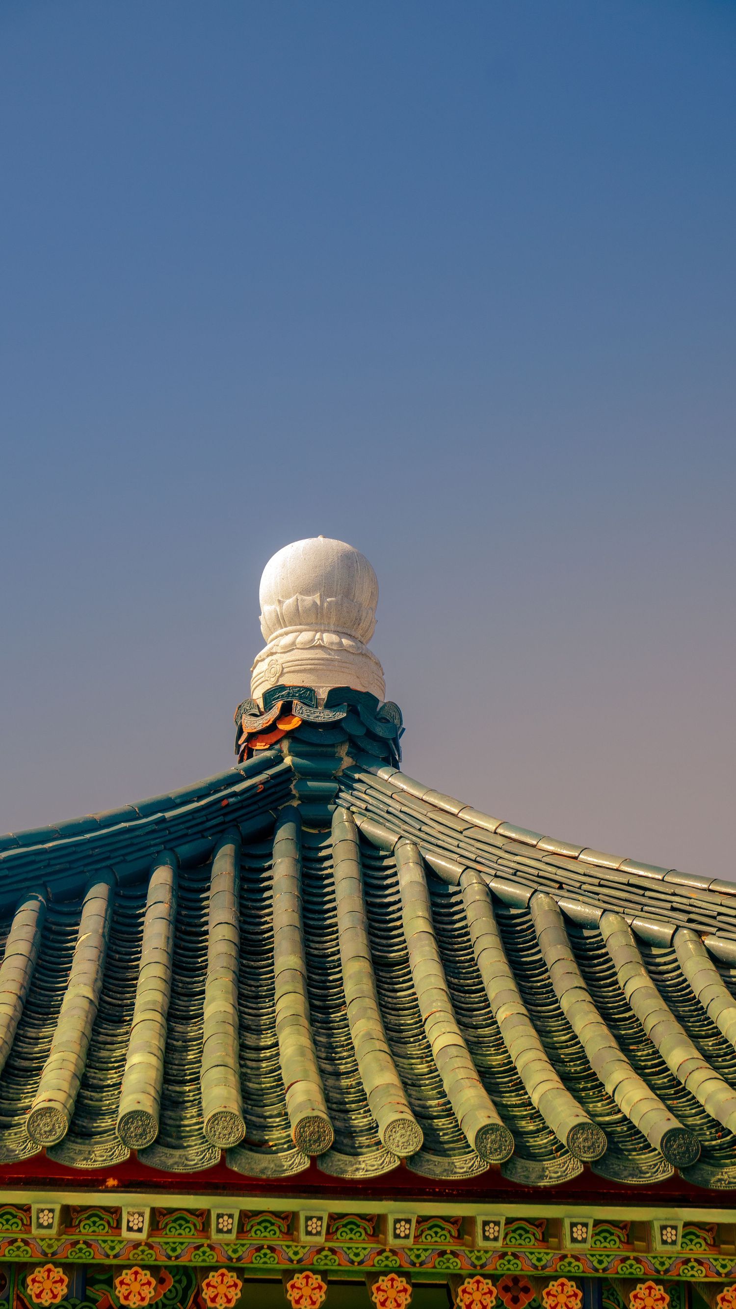 Traditional Korean temple roof tiles with white ornamental finial against blue sky.