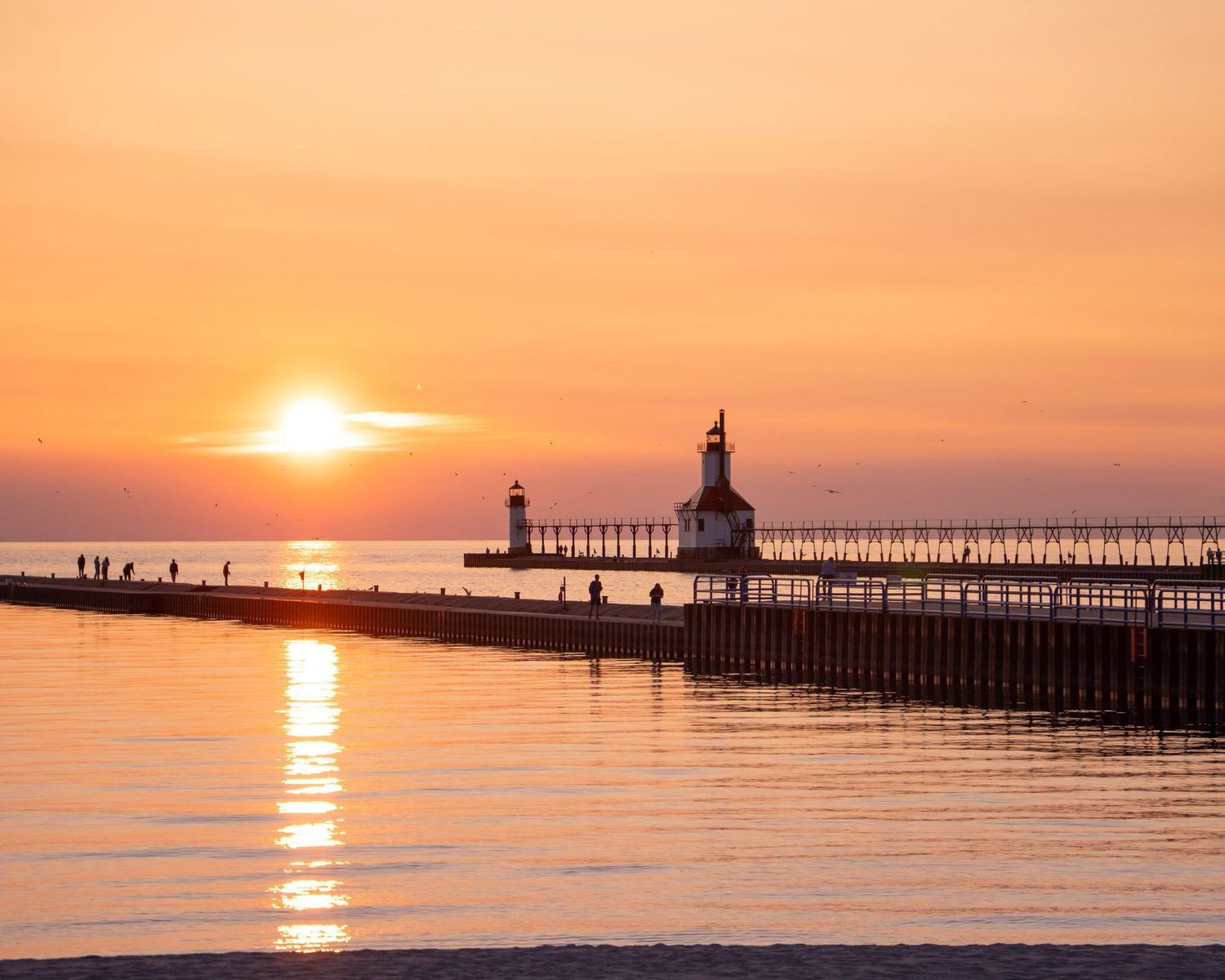 St. Joseph lighthouse and pier silhouetted against dramatic orange sunset over Lake Michigan.