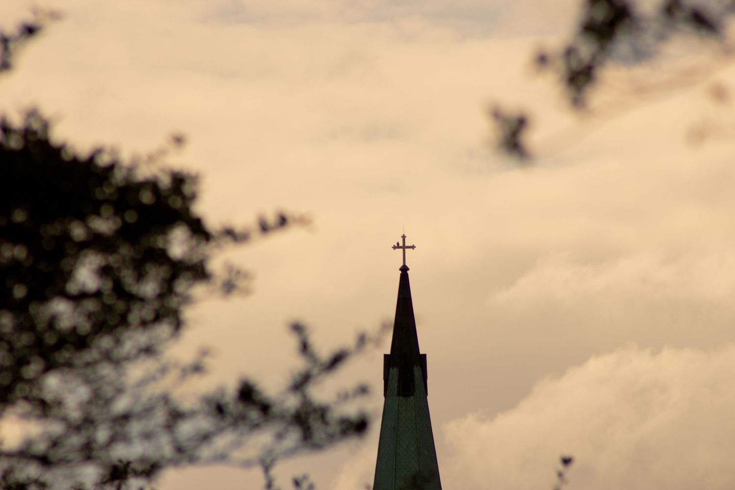 Church spire with cross silhouetted against cloudy sky.