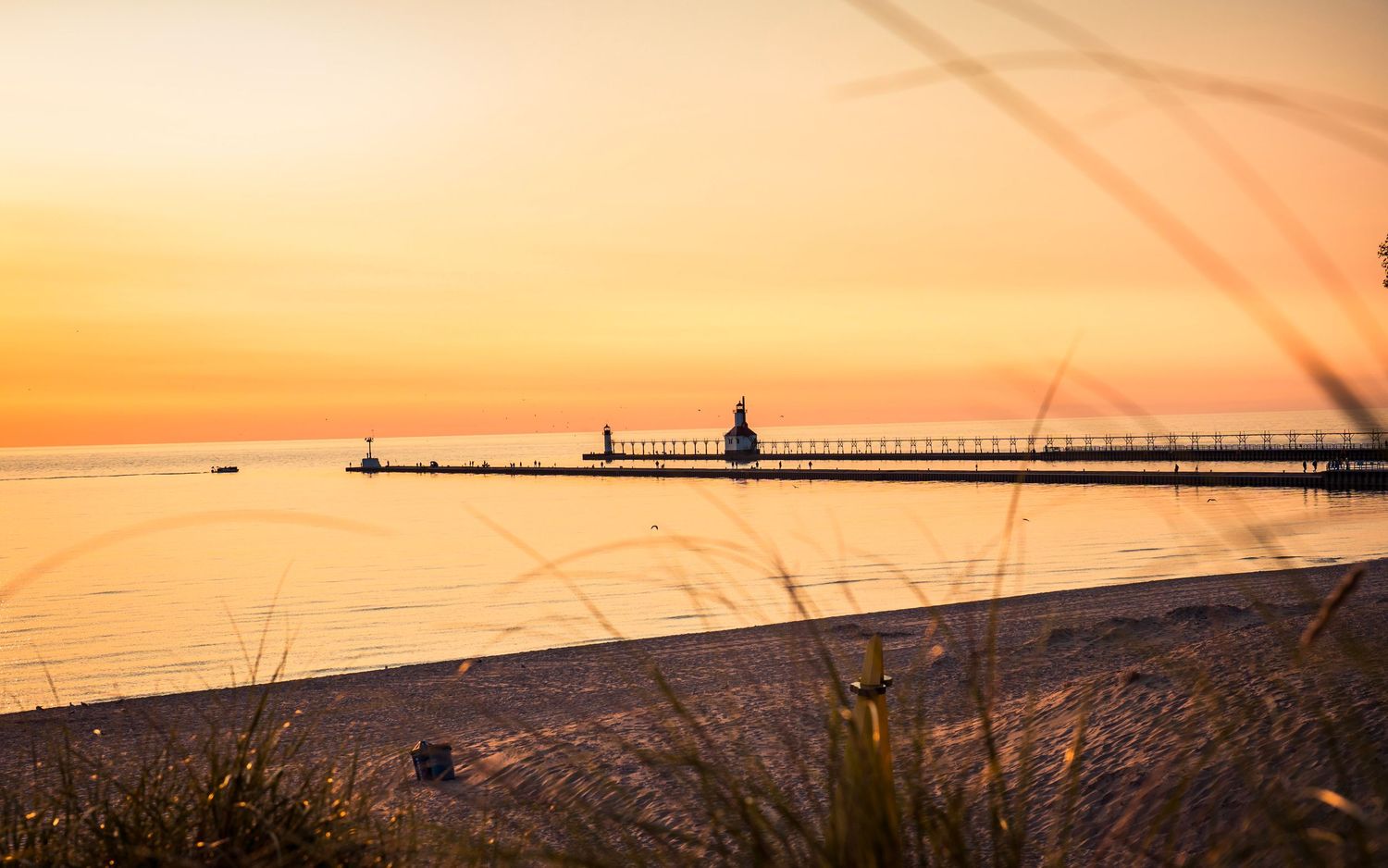 Long pier stretches into Lake Michigan during a vibrant orange sunset over the calm waters.