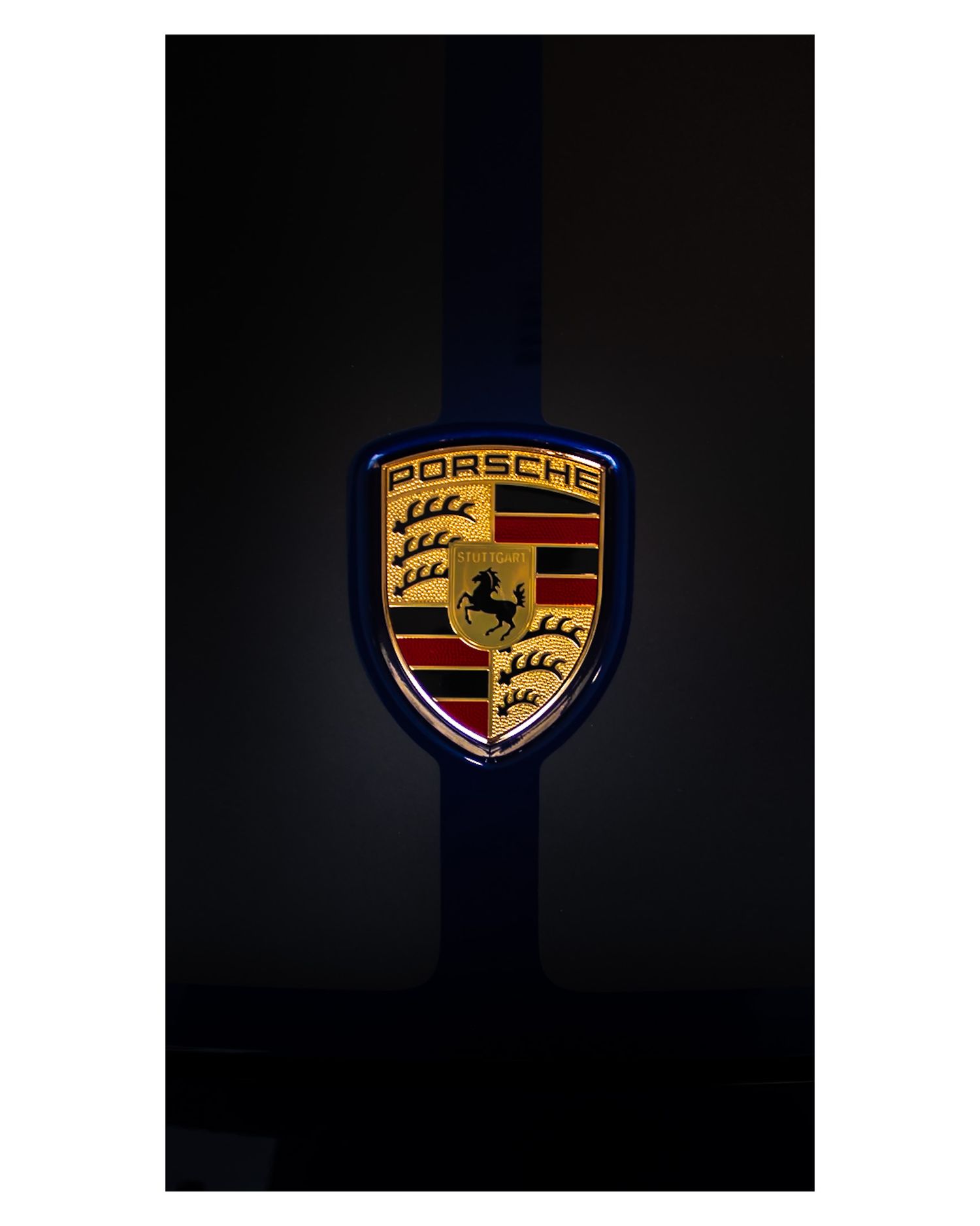Illuminated gold and black Porsche logo emblem against a dark background.
