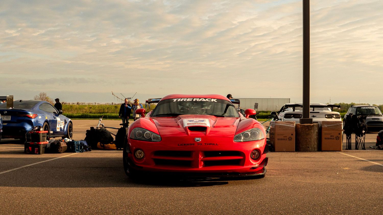 Front view of a red Dodge Viper at sunset in a parking lot with other cars visible.